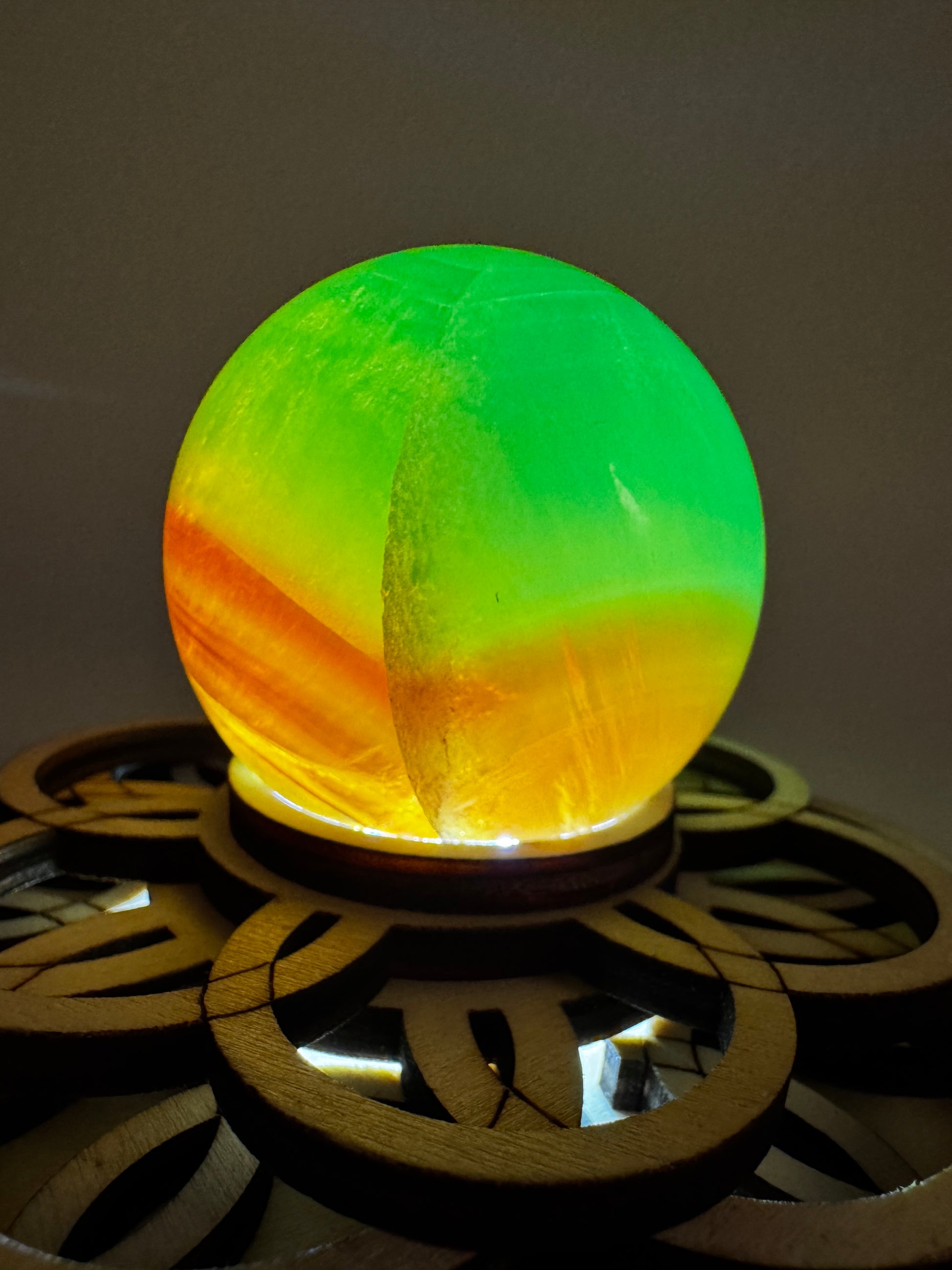 Eine  Fluorit-Kugel in Grün und Orange auf einem Leuchtsockel.