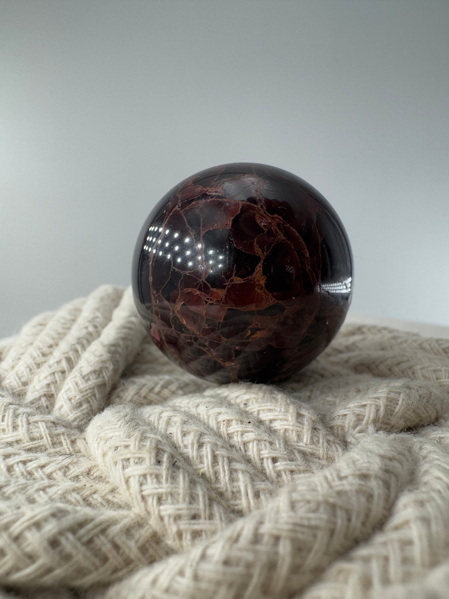 Eine polierte Kugel aus tiefrotem Granat  zeigt unter punktuellem Licht seidige Reflexionen sowie die typische mineralische Textur.