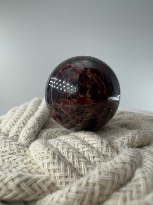 Eine polierte Kugel aus tiefrotem Granat  zeigt unter punktuellem Licht seidige Reflexionen sowie die typische mineralische Textur.