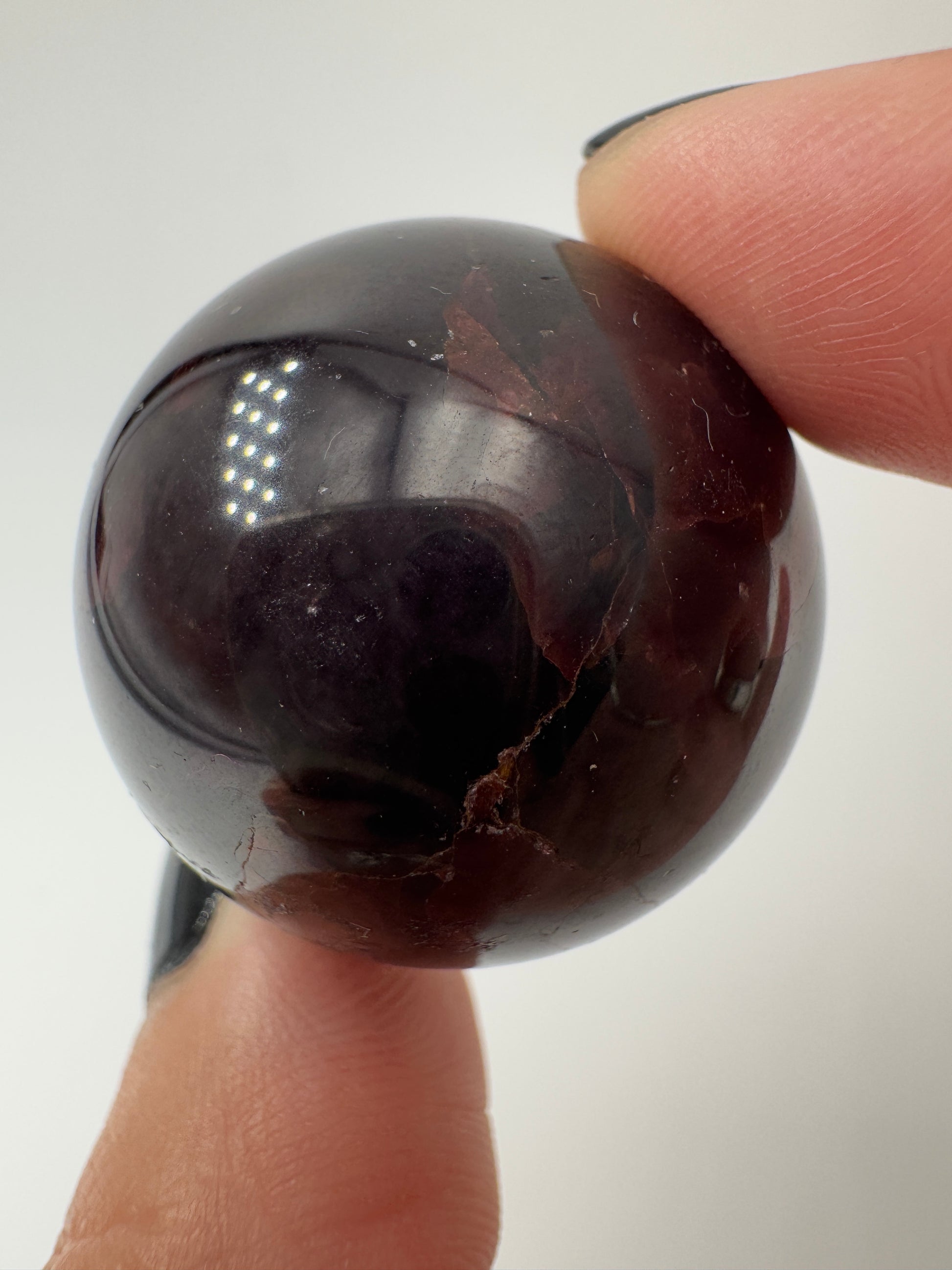 Eine polierte Kugel aus tiefrotem Granat  zeigt unter punktuellem Licht seidige Reflexionen sowie die typische mineralische Textur.