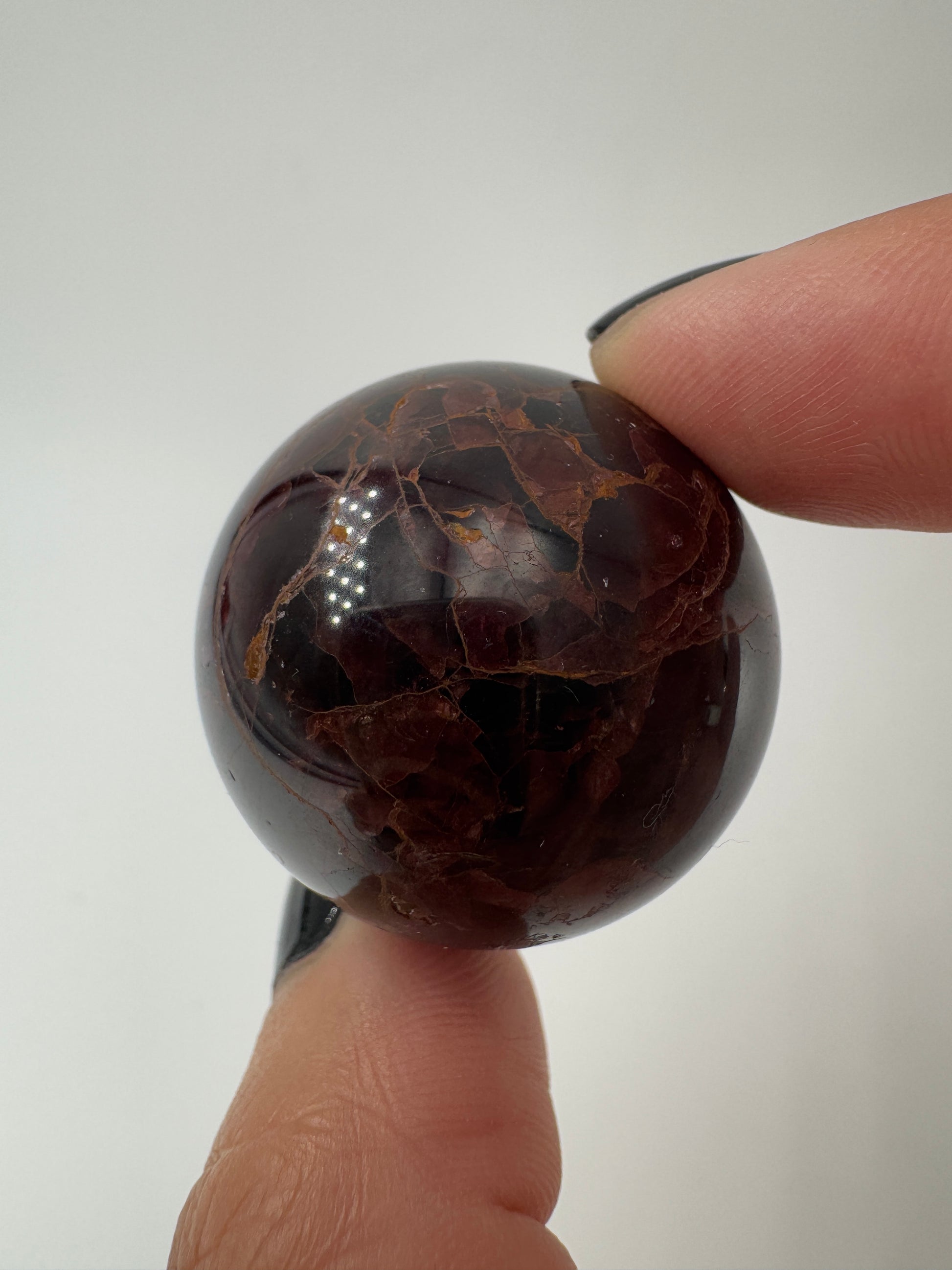 Eine polierte Kugel aus tiefrotem Granat  zeigt unter punktuellem Licht seidige Reflexionen sowie die typische mineralische Textur.