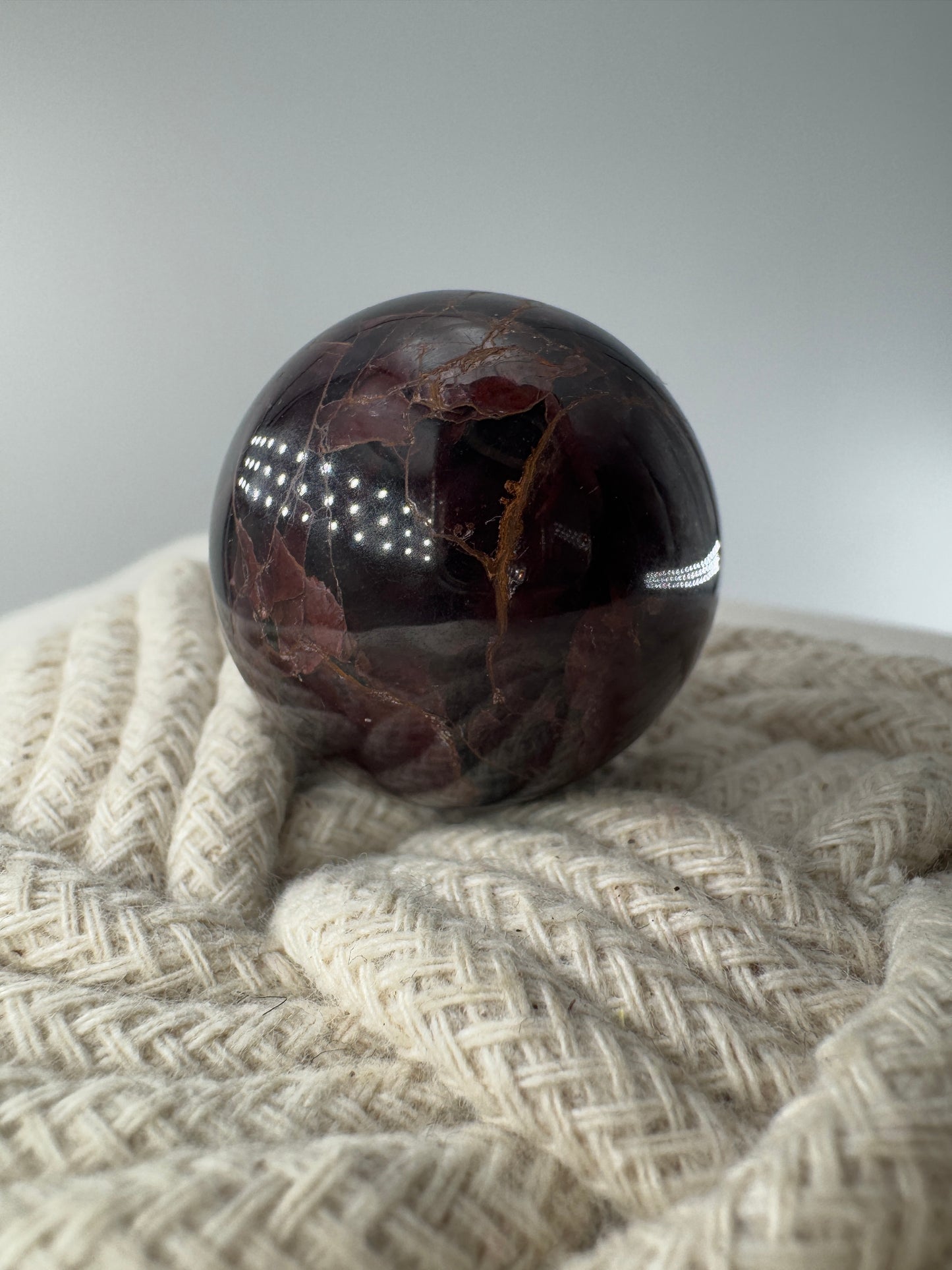 Eine polierte Kugel aus tiefrotem Granat  zeigt unter punktuellem Licht seidige Reflexionen sowie die typische mineralische Textur.