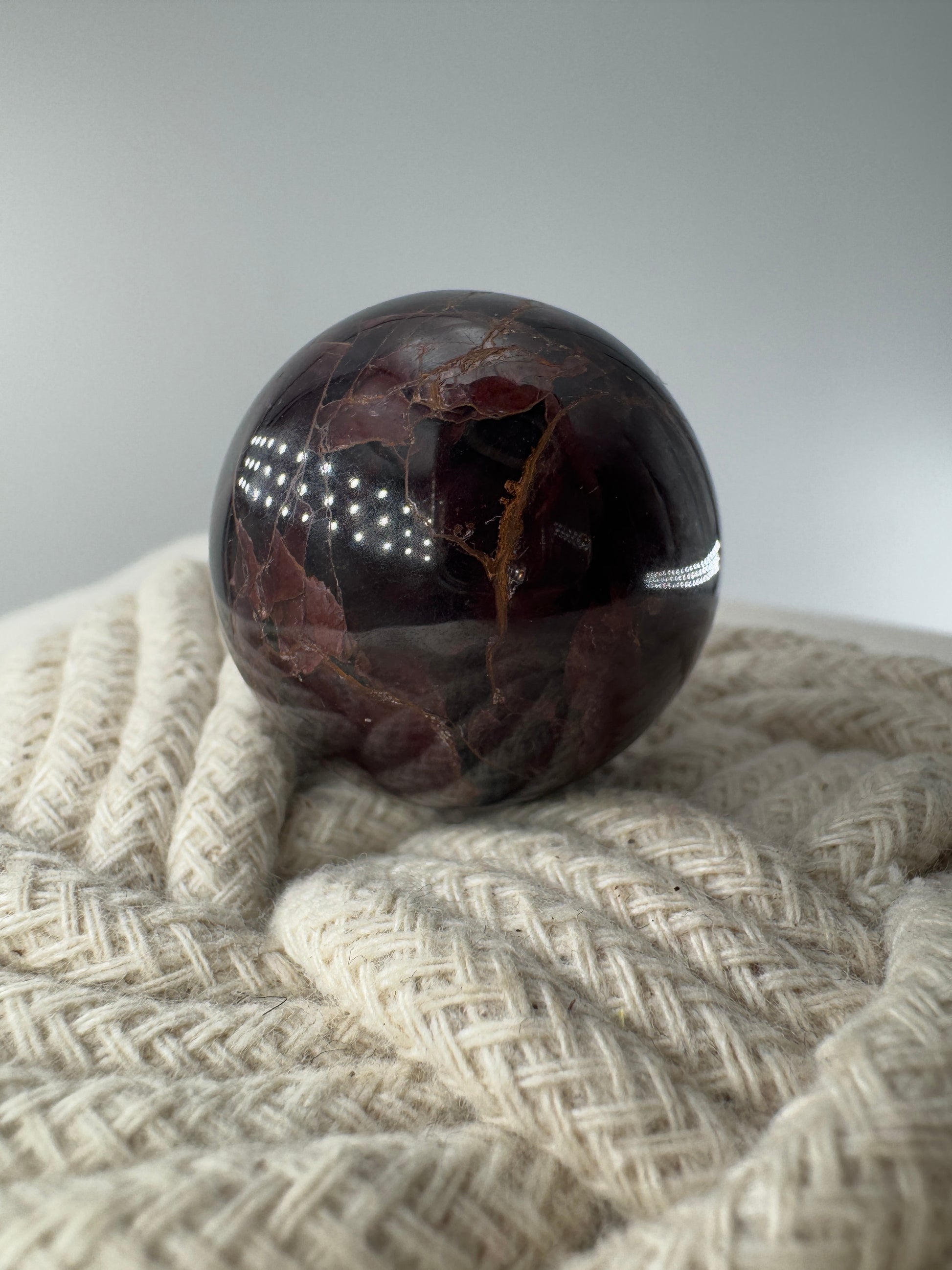 Eine polierte Kugel aus tiefrotem Granat  zeigt unter punktuellem Licht seidige Reflexionen sowie die typische mineralische Textur.