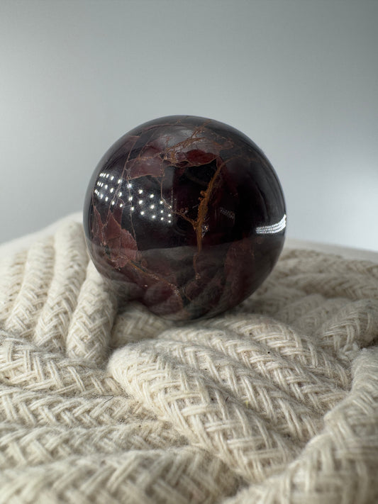 Eine polierte Kugel aus tiefrotem Granat  zeigt unter punktuellem Licht seidige Reflexionen sowie die typische mineralische Textur.