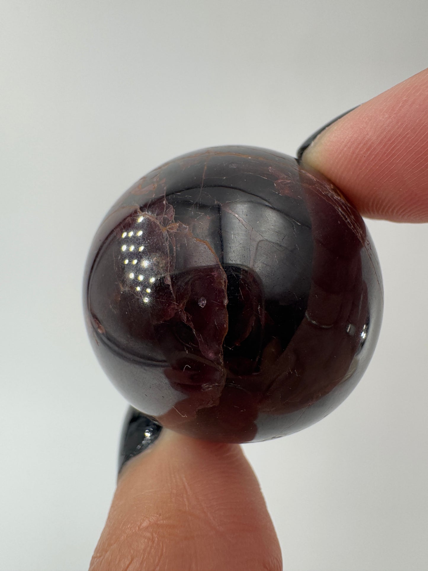 Eine polierte Kugel aus tiefrotem Granat  zeigt unter punktuellem Licht seidige Reflexionen sowie die typische mineralische Textur.