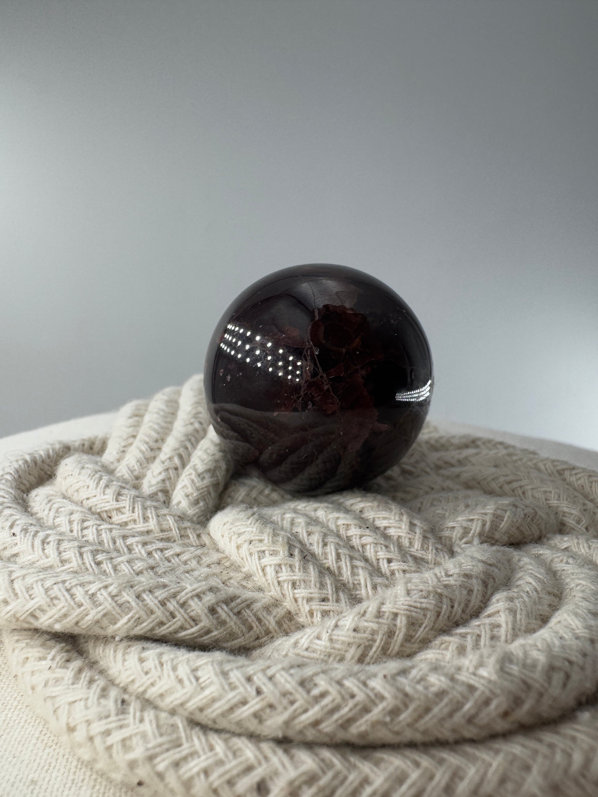 Eine polierte Kugel aus tiefrotem Granat  zeigt unter punktuellem Licht seidige Reflexionen sowie die typische mineralische Textur.