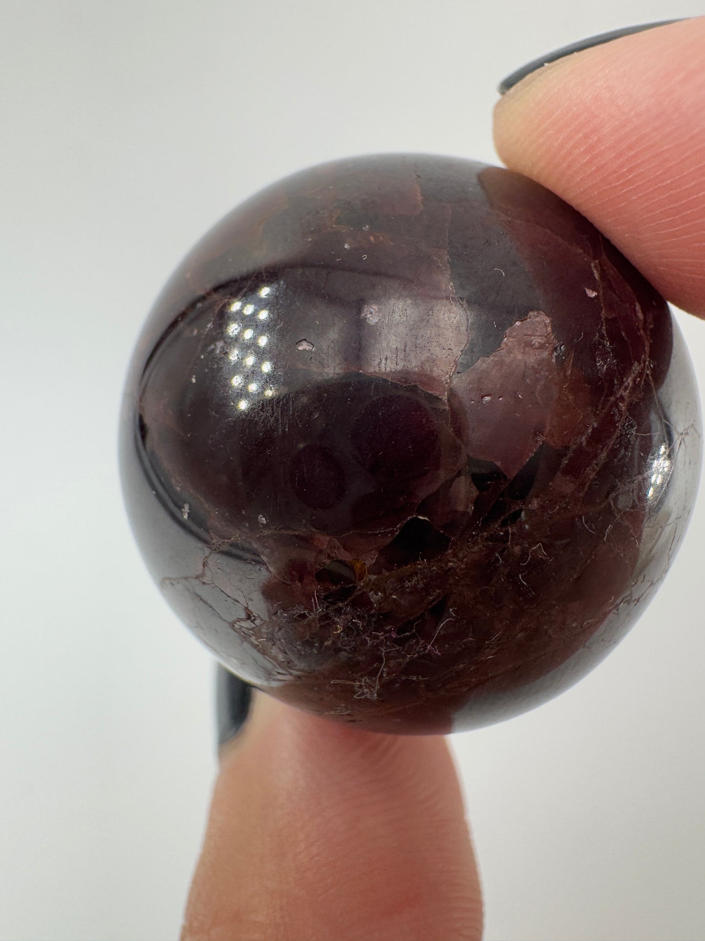 Eine polierte Kugel aus tiefrotem Granat  zeigt unter punktuellem Licht seidige Reflexionen sowie die typische mineralische Textur.