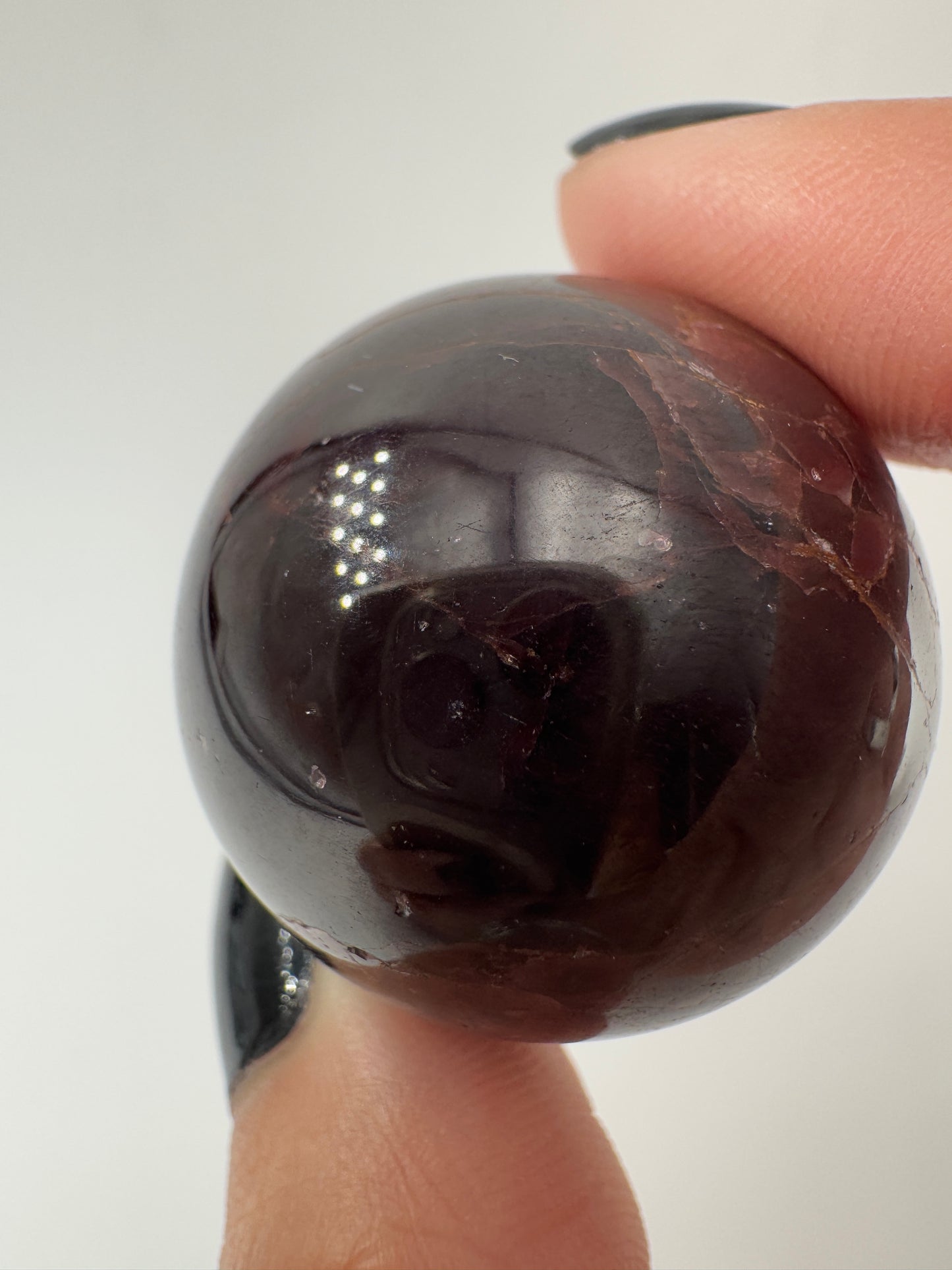 Eine polierte Kugel aus tiefrotem Granat  zeigt unter punktuellem Licht seidige Reflexionen sowie die typische mineralische Textur.