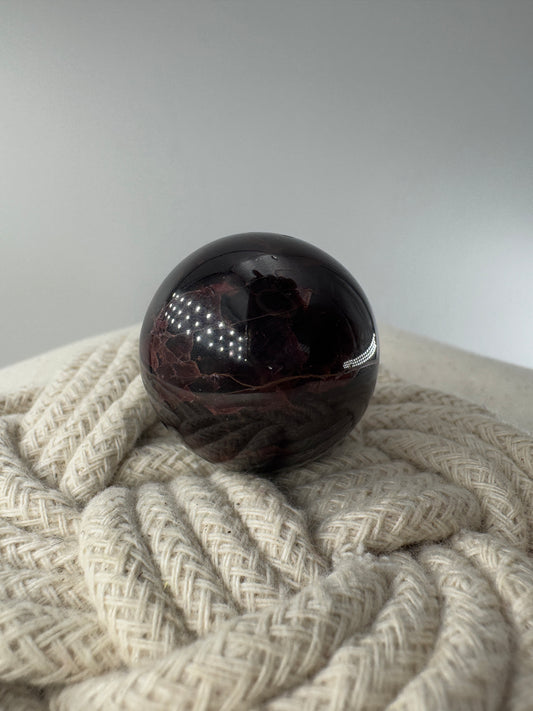 Eine polierte Kugel aus tiefrotem Granat  zeigt unter punktuellem Licht seidige Reflexionen sowie die typische mineralische Textur.