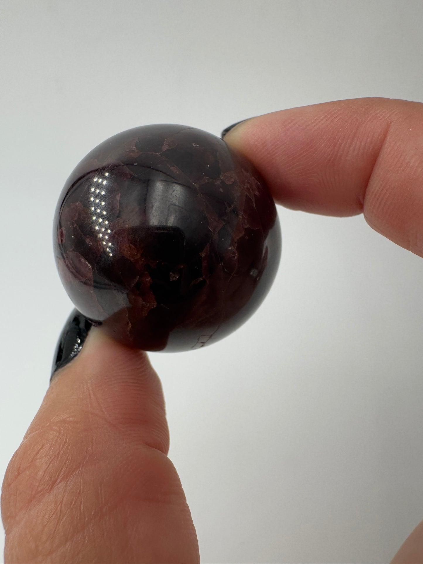 Eine polierte Kugel aus tiefrotem Granat  zeigt unter punktuellem Licht seidige Reflexionen sowie die typische mineralische Textur.