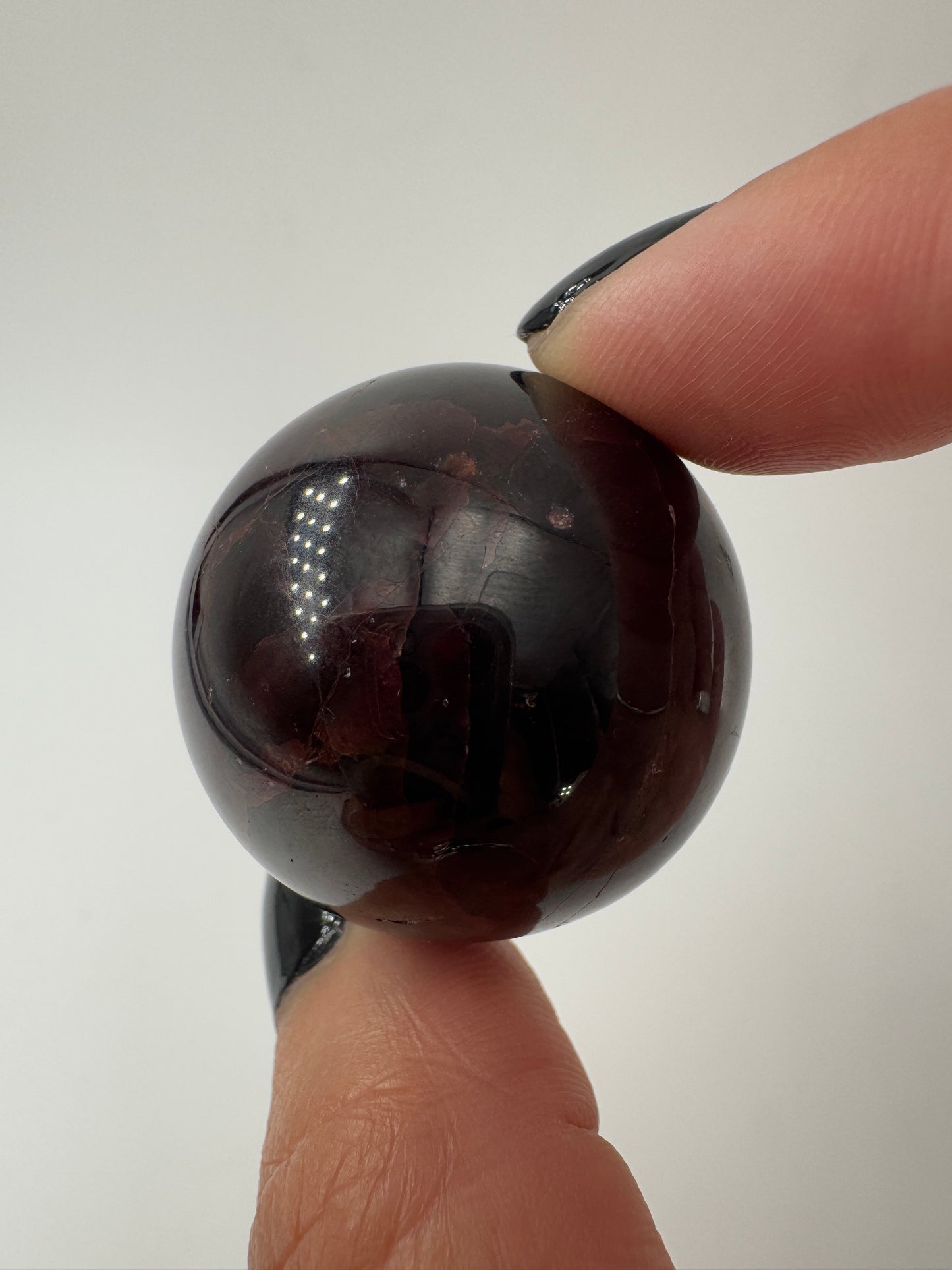 Eine polierte Kugel aus tiefrotem Granat  zeigt unter punktuellem Licht seidige Reflexionen sowie die typische mineralische Textur.