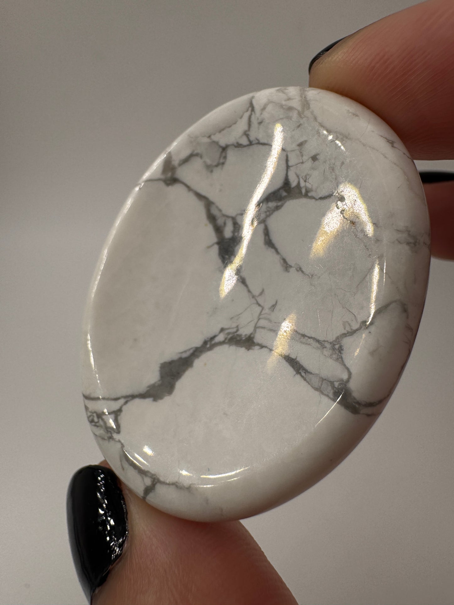 Ein  Daumensteinen aus Howlit mit glänzend polierten Oberflächen und zentraler Daumenmulde.