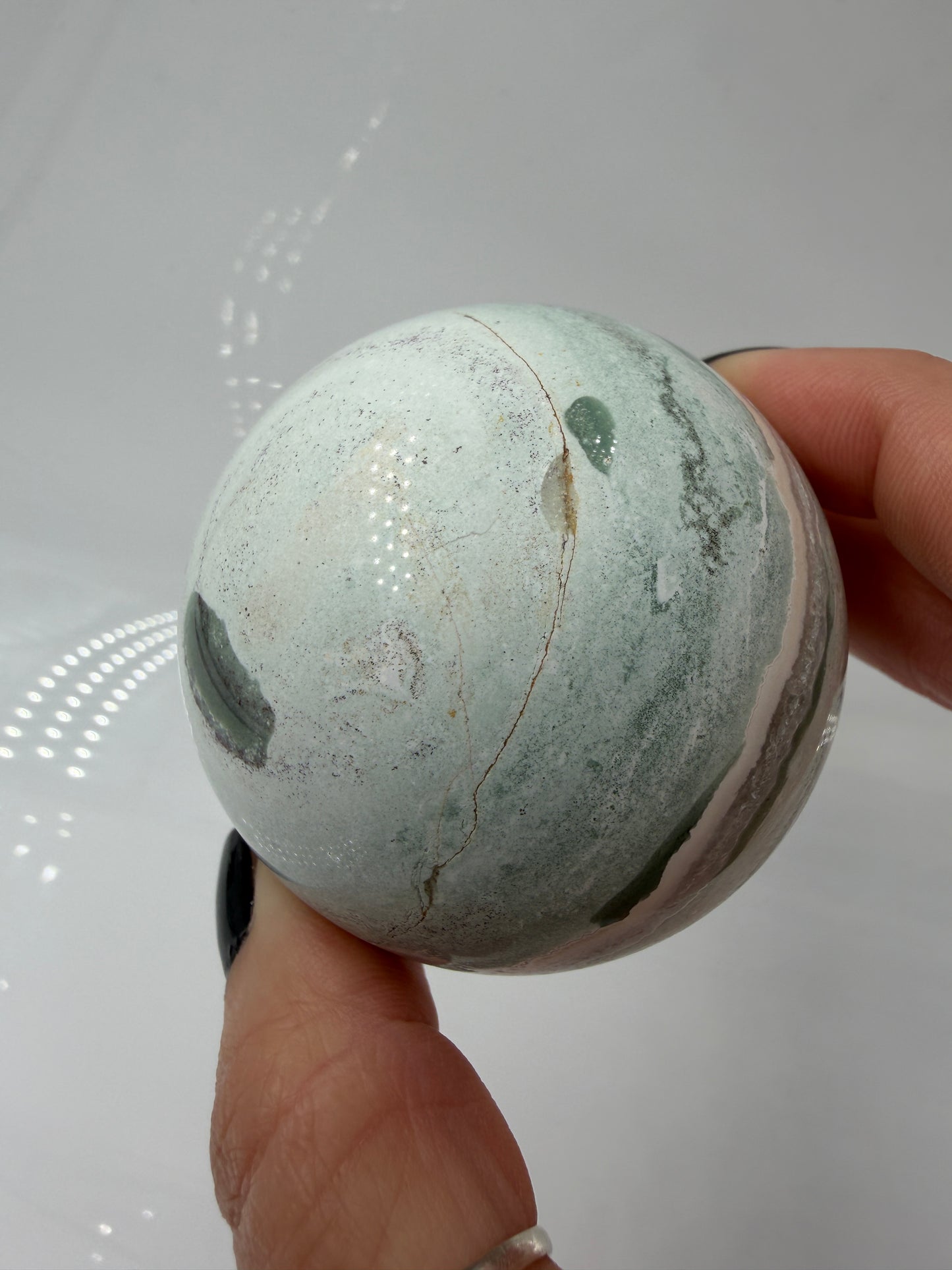 Eine perfekt polierte Kugel aus indischem Jaspis mit einem lebhaften Muster aus grünem und weißen Mineralbändern, die eine faszinierende, natürliche Textur bilden.