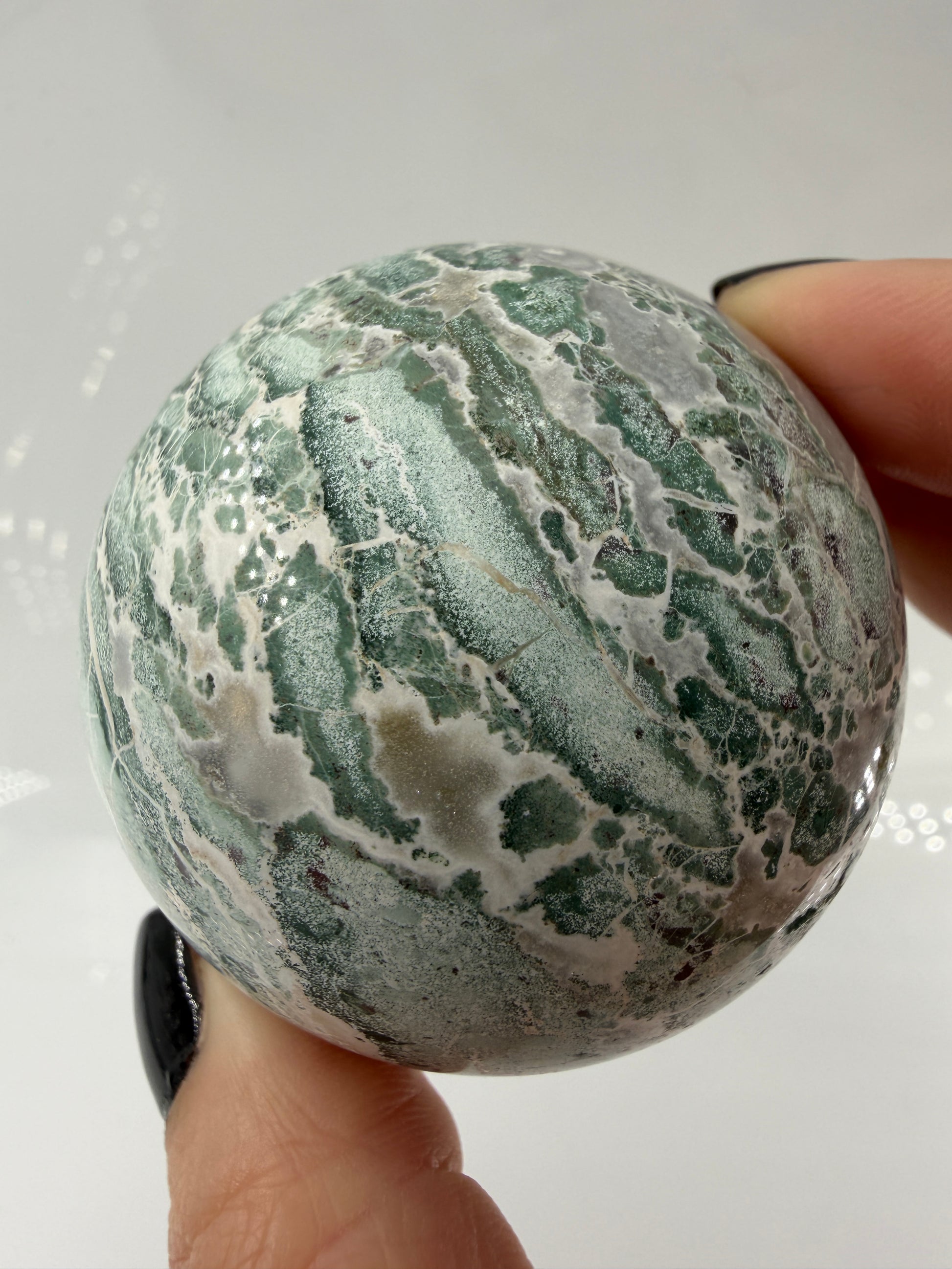Eine perfekt polierte Kugel aus indischem Jaspis mit einem lebhaften Muster aus grünem und weißen Mineralbändern, die eine faszinierende, natürliche Textur bilden.