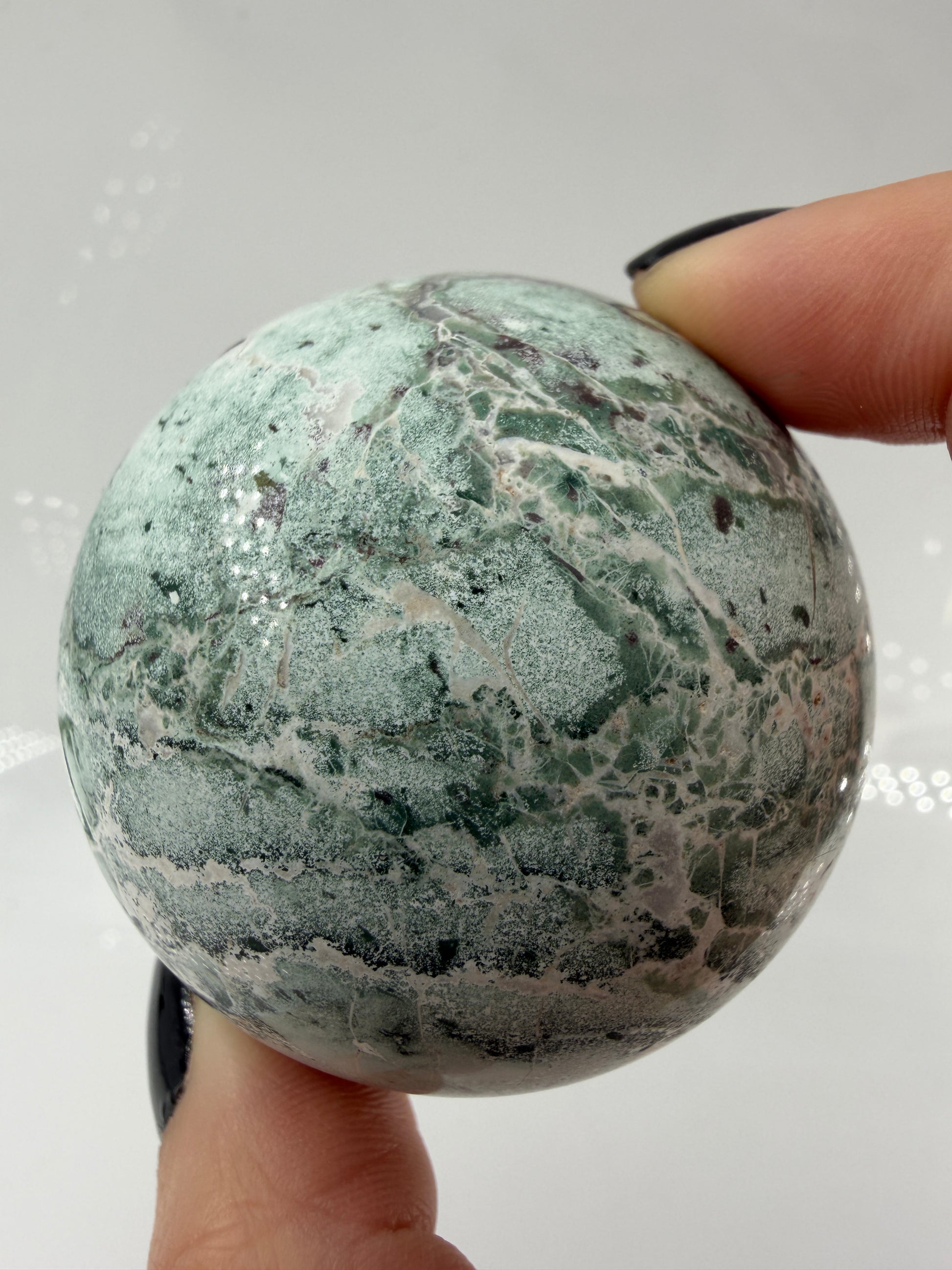 Eine perfekt polierte Kugel aus indischem Jaspis mit einem lebhaften Muster aus grünem und weißen Mineralbändern, die eine faszinierende, natürliche Textur bilden.