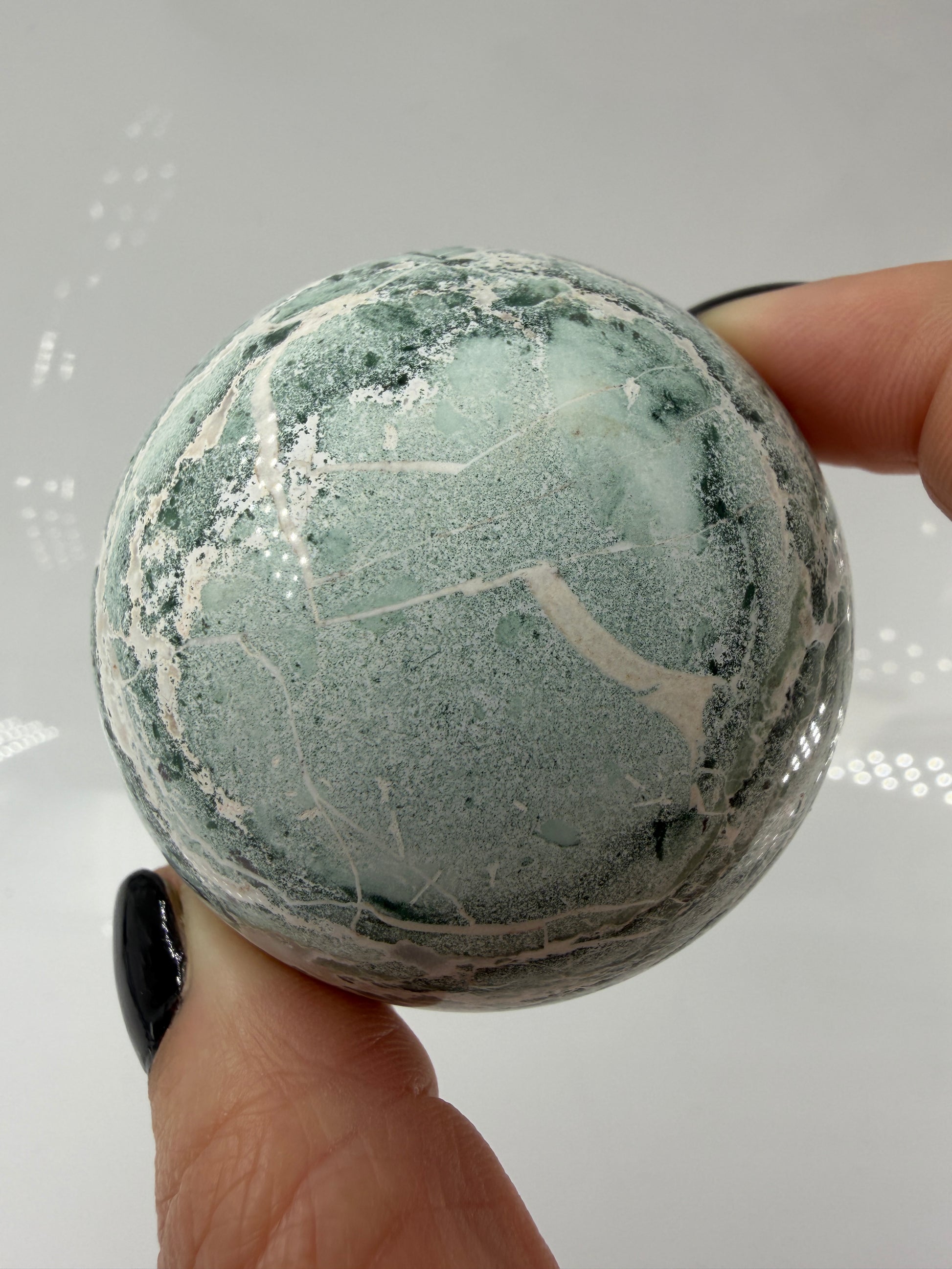 Eine perfekt polierte Kugel aus indischem Jaspis mit einem lebhaften Muster aus grünem und weißen Mineralbändern, die eine faszinierende, natürliche Textur bilden.