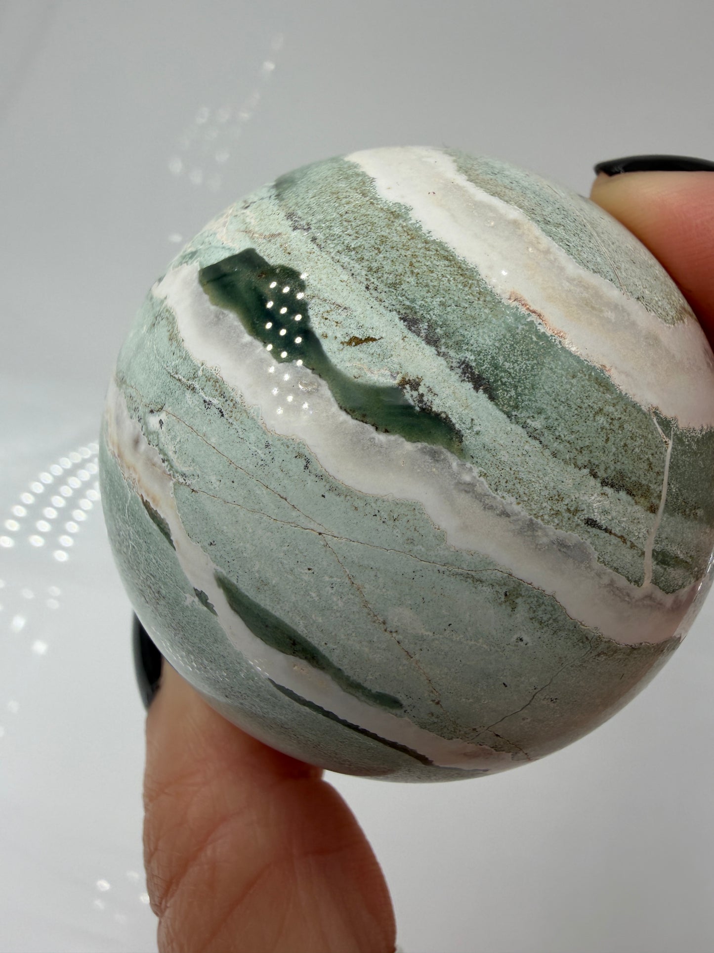 Eine perfekt polierte Kugel aus indischem Jaspis mit einem lebhaften Muster aus grünem und weißen Mineralbändern, die eine faszinierende, natürliche Textur bilden.