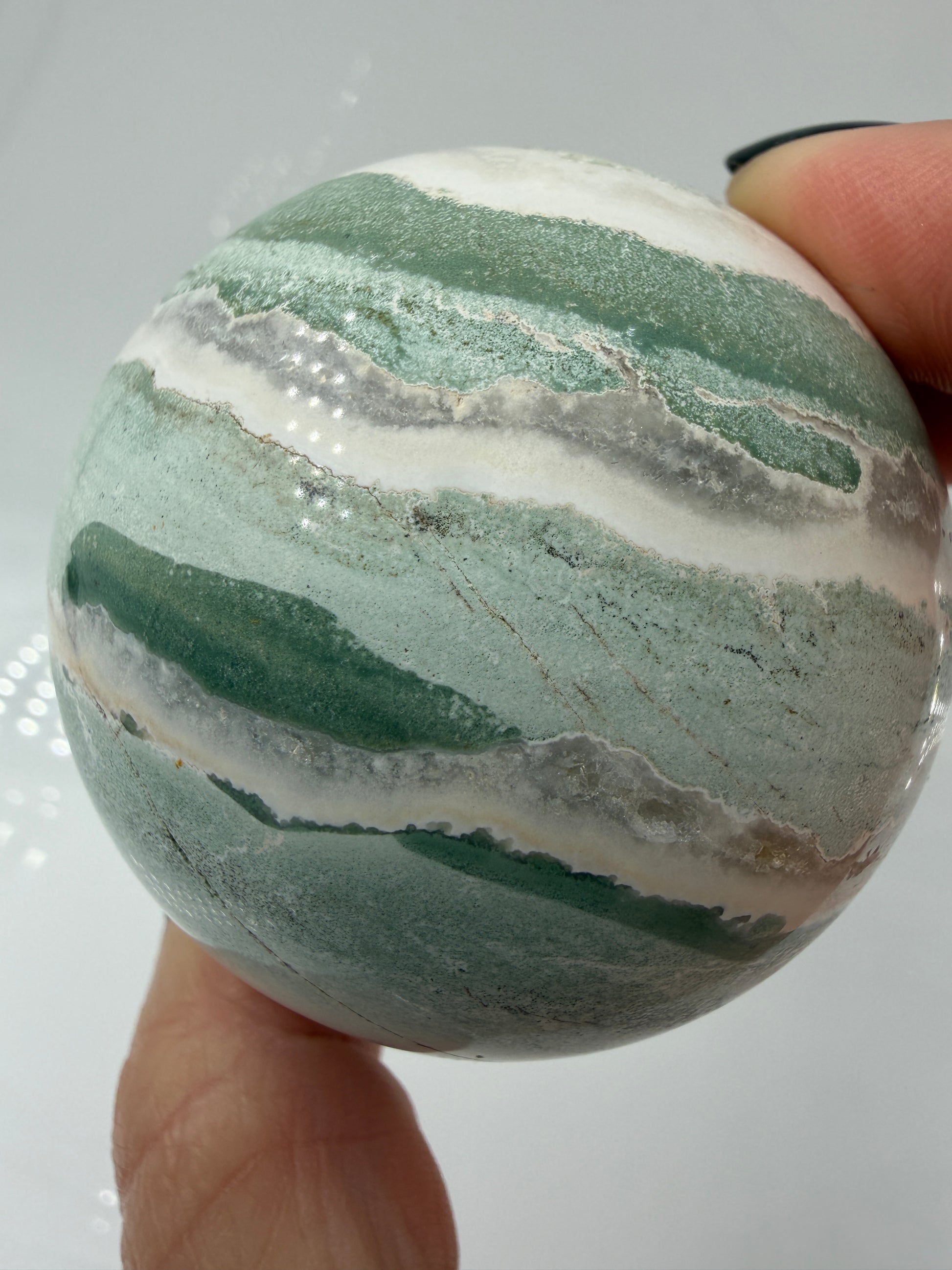 Eine perfekt polierte Kugel aus indischem Jaspis mit einem lebhaften Muster aus grünem und weißen Mineralbändern, die eine faszinierende, natürliche Textur bilden.