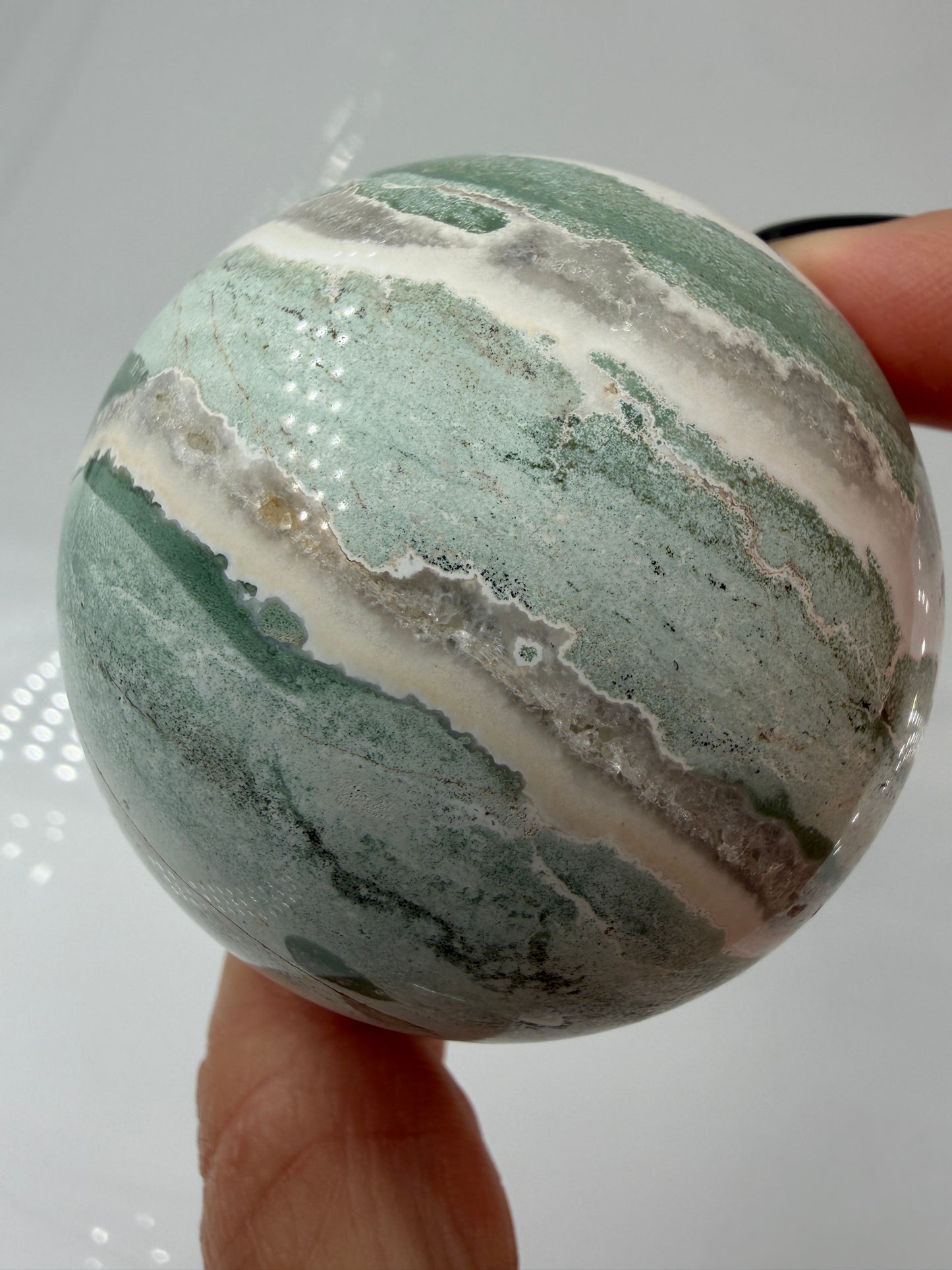 Eine perfekt polierte Kugel aus indischem Jaspis mit einem lebhaften Muster aus grünem und weißen Mineralbändern, die eine faszinierende, natürliche Textur bilden.