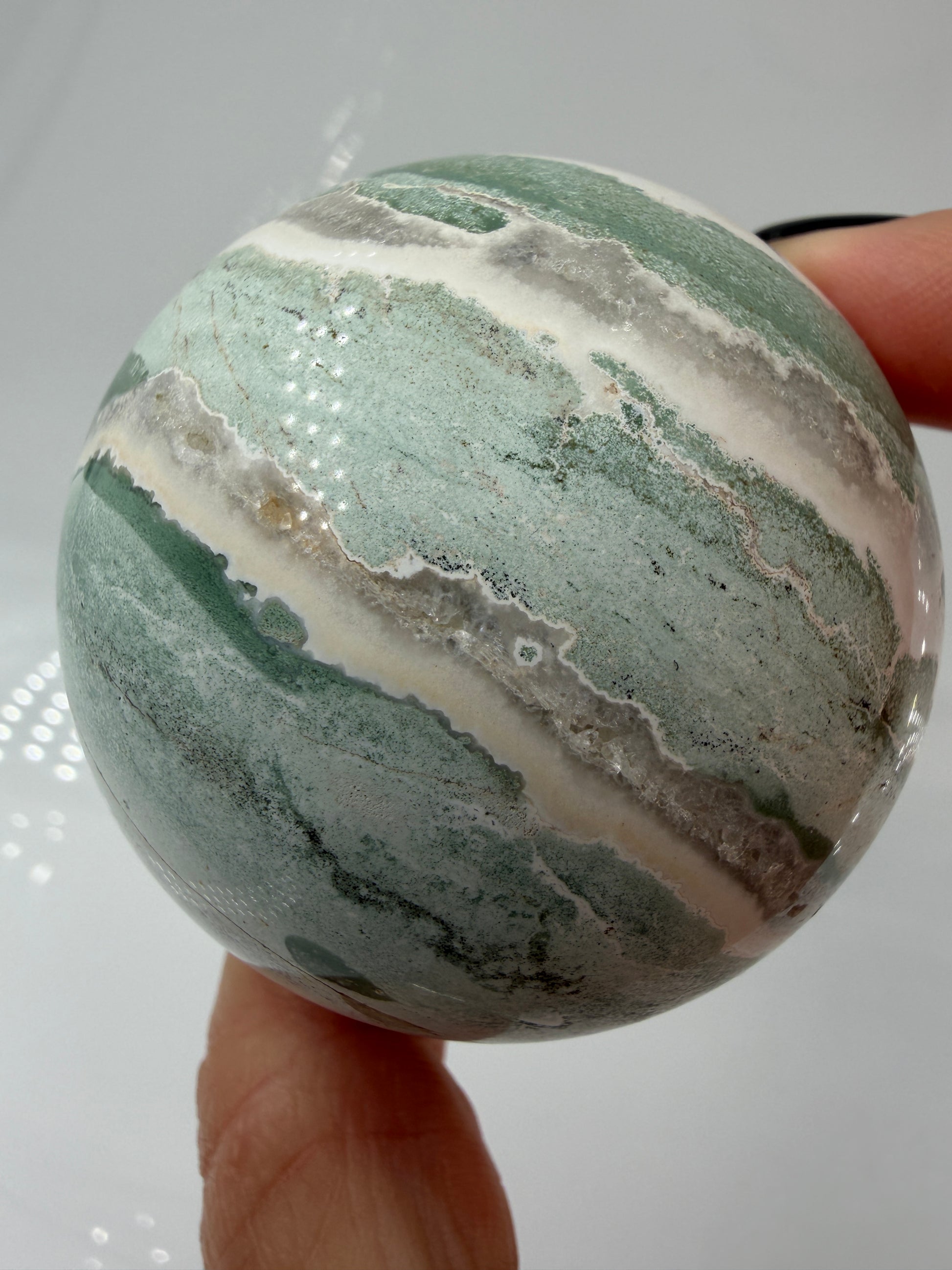 Eine perfekt polierte Kugel aus indischem Jaspis mit einem lebhaften Muster aus grünem und weißen Mineralbändern, die eine faszinierende, natürliche Textur bilden.