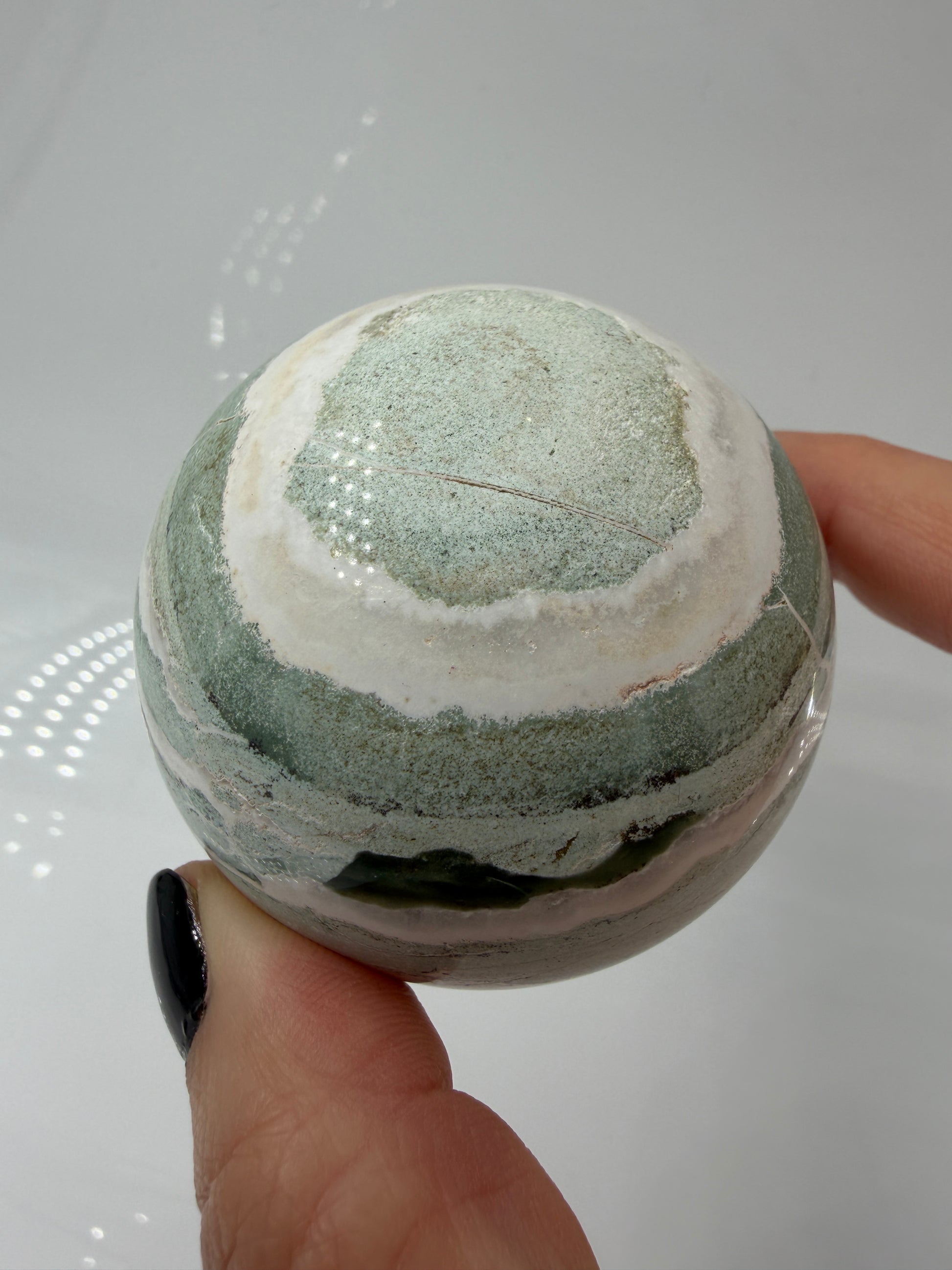 Eine perfekt polierte Kugel aus indischem Jaspis mit einem lebhaften Muster aus grünem und weißen Mineralbändern, die eine faszinierende, natürliche Textur bilden.