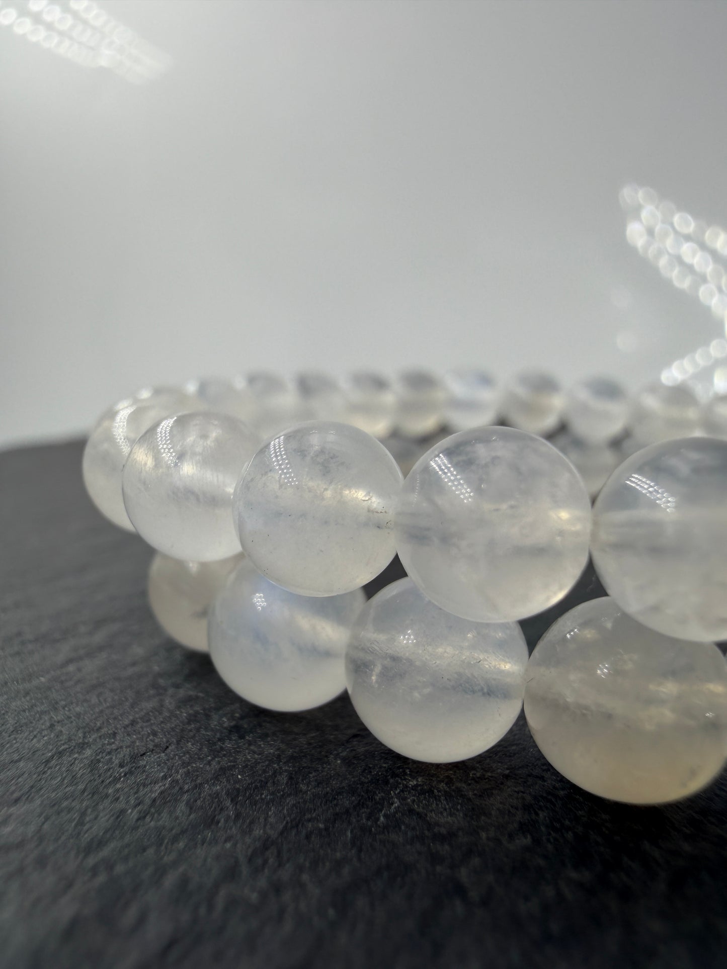 Ein elegantes Armband aus polierten, weiß-transparenten Labradorit-Kugeln, die bei Lichteinfall einen intensiven, elektrisch blauen Schimmer auf ihrer Oberfläche zeigen.