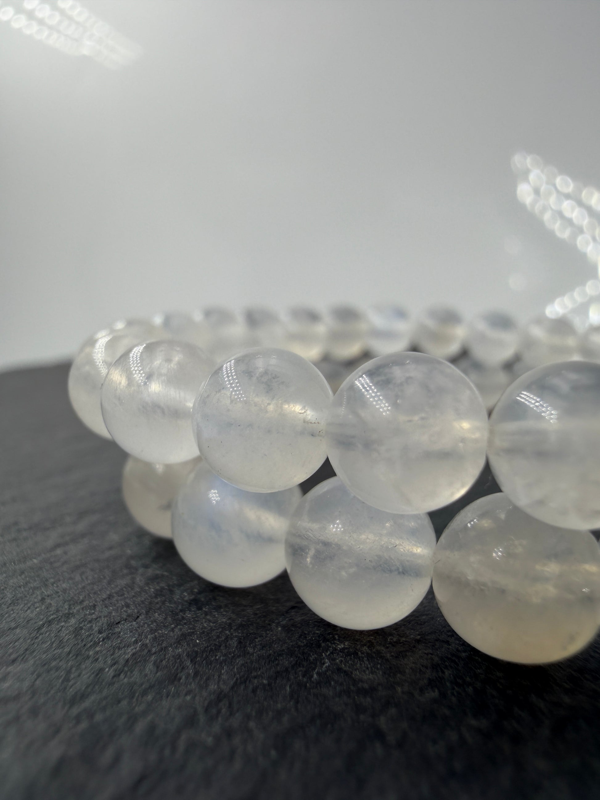 Ein elegantes Armband aus polierten, weiß-transparenten Labradorit-Kugeln, die bei Lichteinfall einen intensiven, elektrisch blauen Schimmer auf ihrer Oberfläche zeigen.