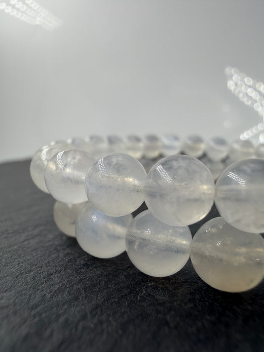 Ein elegantes Armband aus polierten, weiß-transparenten Labradorit-Kugeln, die bei Lichteinfall einen intensiven, elektrisch blauen Schimmer auf ihrer Oberfläche zeigen.