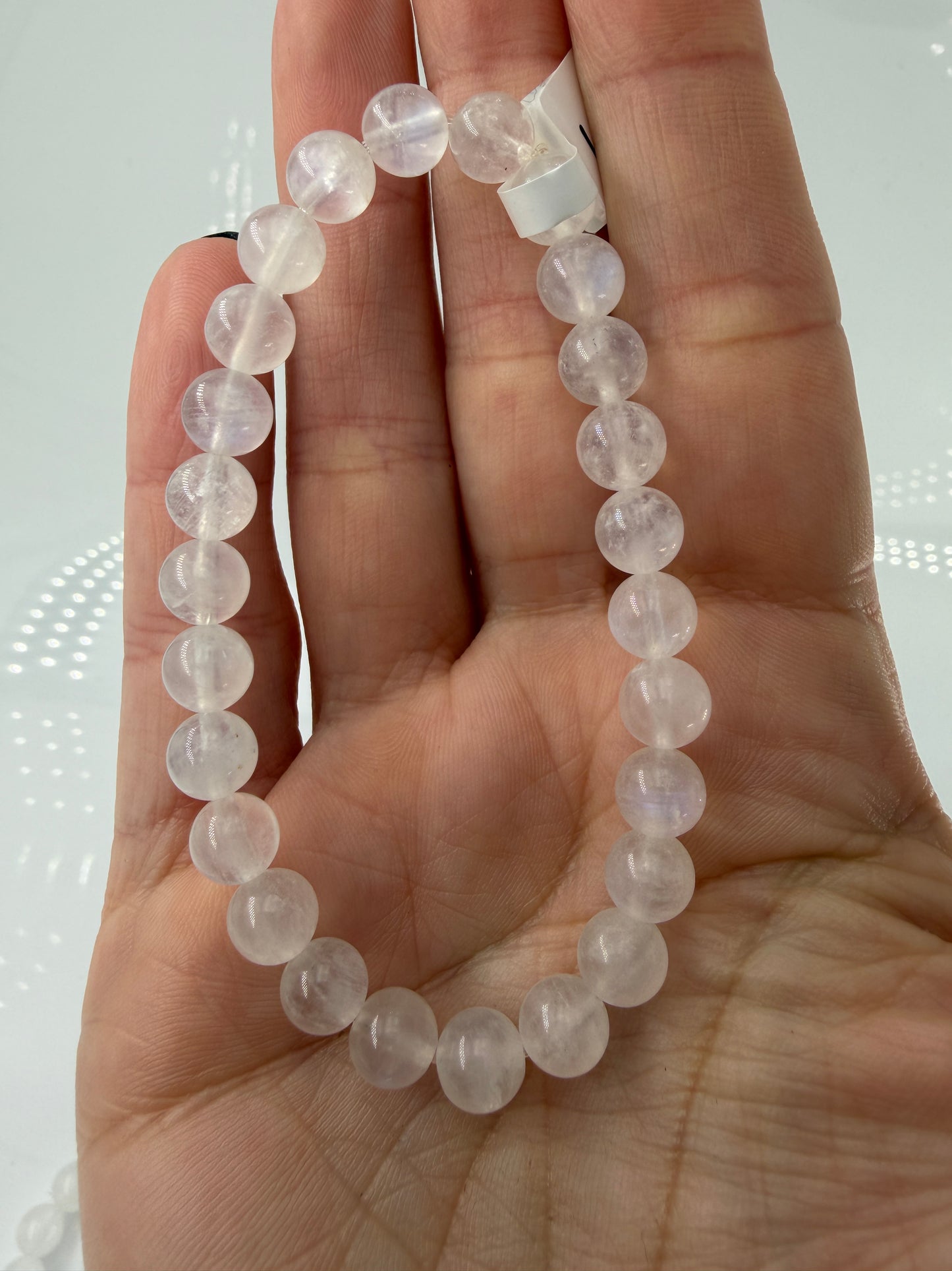 Ein elegantes Armband aus polierten, weiß-transparenten Labradorit-Kugeln, die bei Lichteinfall einen intensiven, elektrisch blauen Schimmer auf ihrer Oberfläche zeigen.