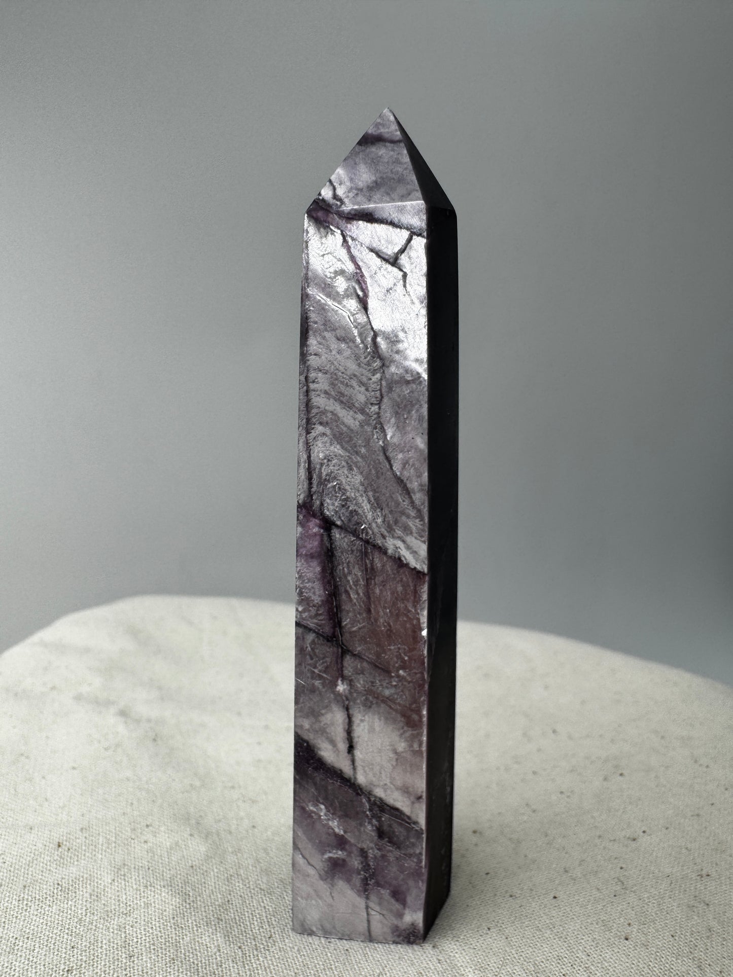 Ein spitz zulaufender, polierter Turm aus fliederfarbenem Lepidolith mit dezent glitzernden Glimmer-Einschlüssen.