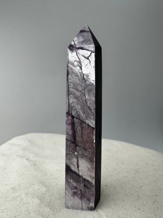 Ein spitz zulaufender, polierter Turm aus fliederfarbenem Lepidolith mit dezent glitzernden Glimmer-Einschlüssen.