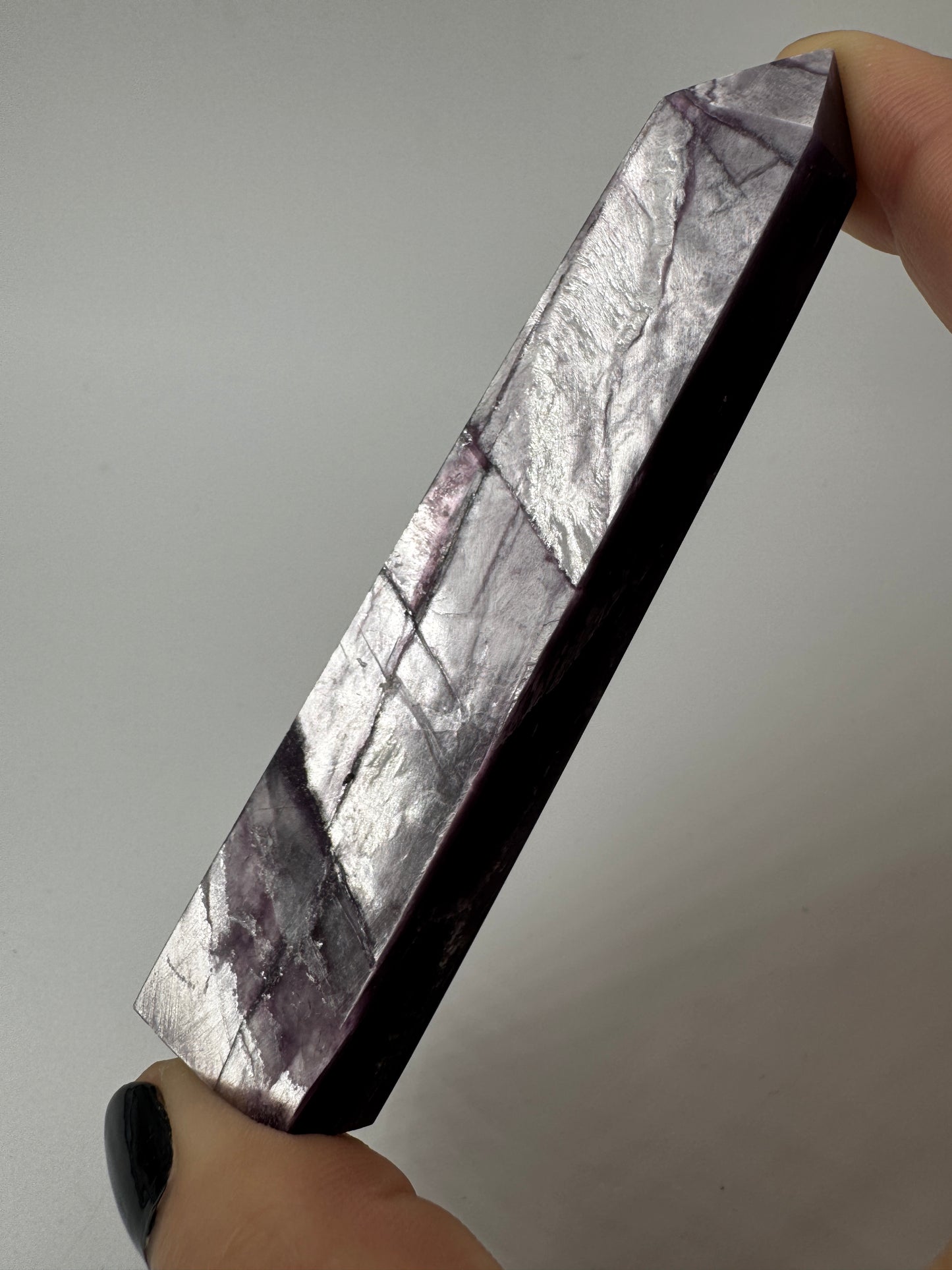 Ein spitz zulaufender, polierter Turm aus fliederfarbenem Lepidolith mit dezent glitzernden Glimmer-Einschlüssen.