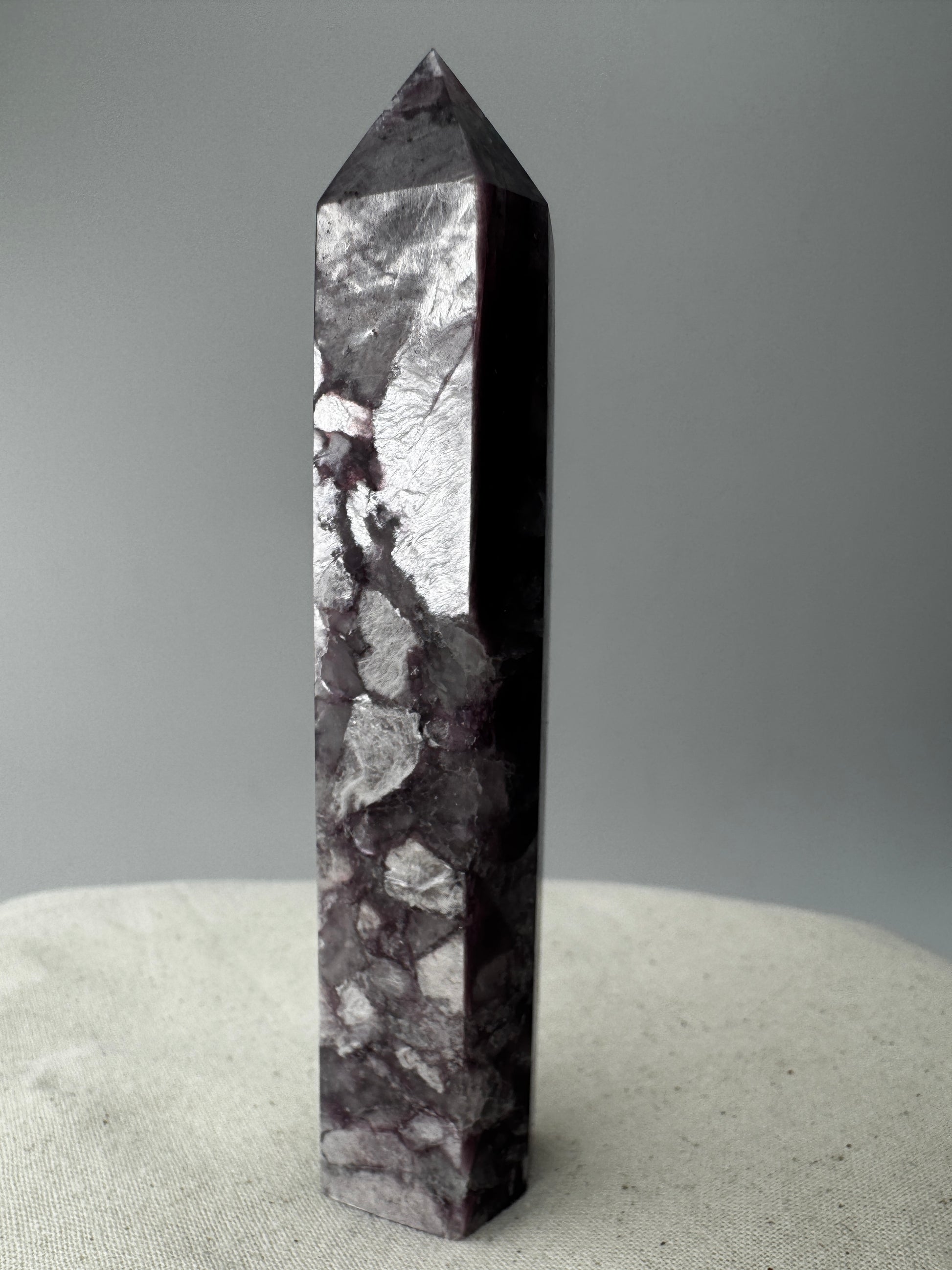Ein spitz zulaufender, polierter Turm aus fliederfarbenem Lepidolith mit dezent glitzernden Glimmer-Einschlüssen