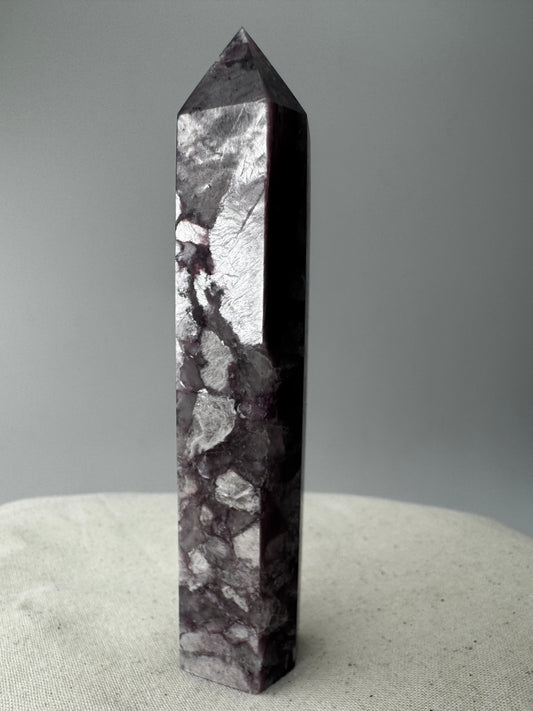 Ein spitz zulaufender, polierter Turm aus fliederfarbenem Lepidolith mit dezent glitzernden Glimmer-Einschlüssen