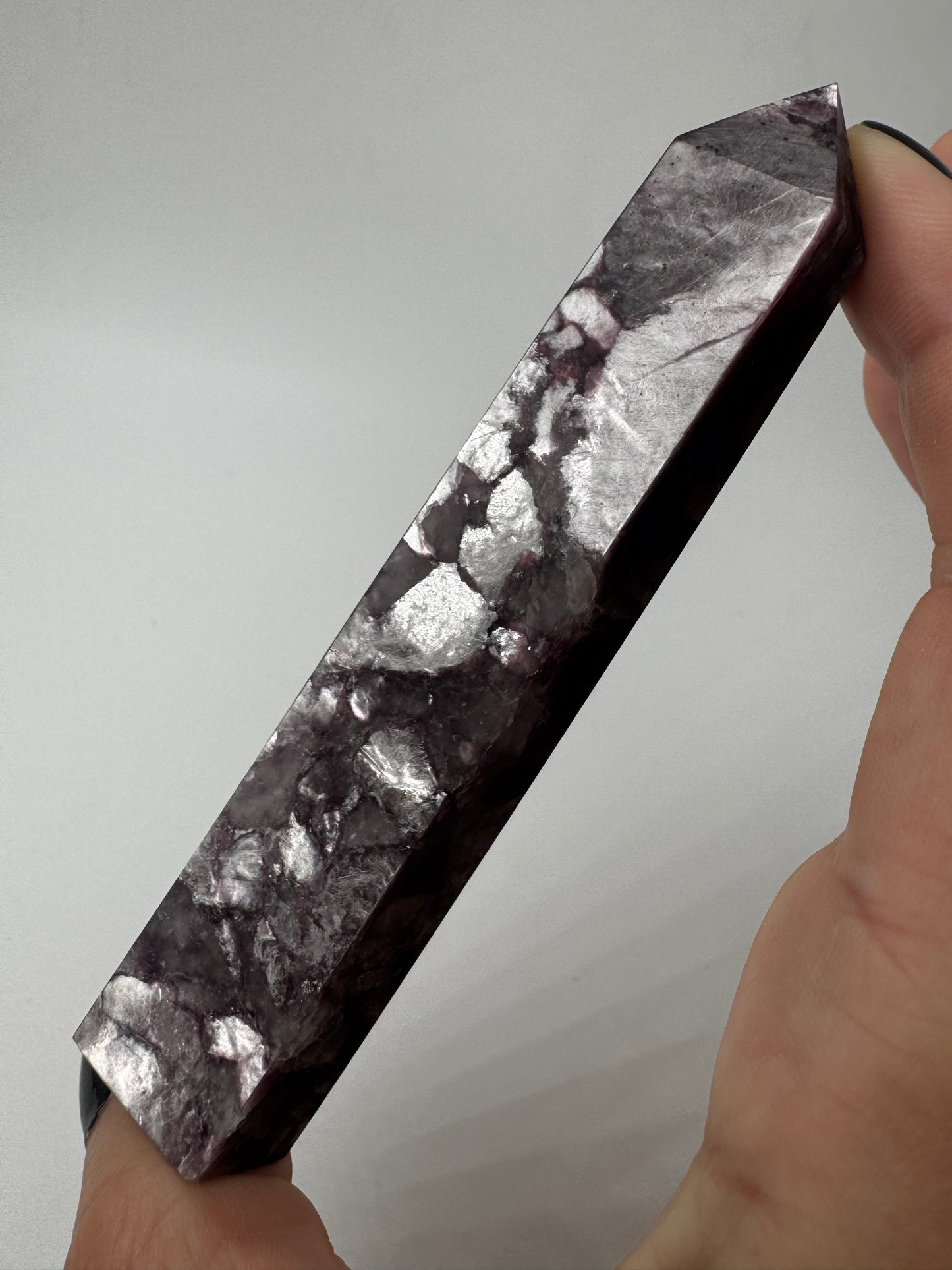 Ein spitz zulaufender, polierter Turm aus fliederfarbenem Lepidolith mit dezent glitzernden Glimmer-Einschlüssen