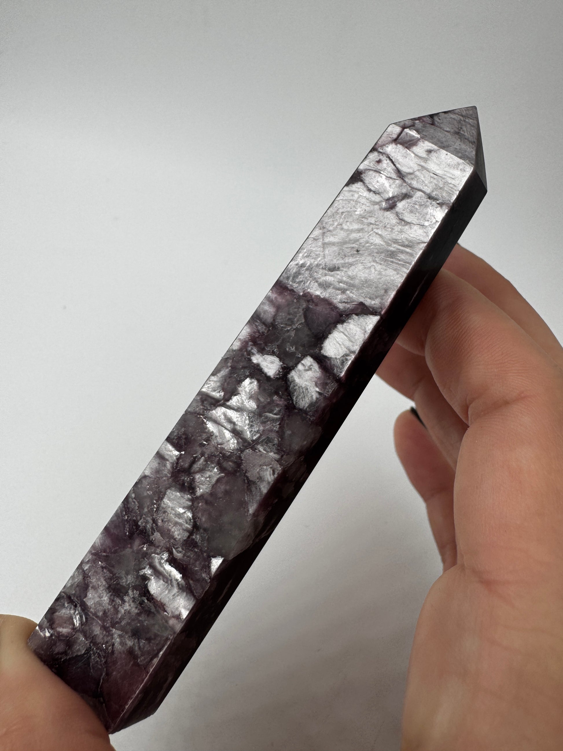 Ein spitz zulaufender, polierter Turm aus fliederfarbenem Lepidolith mit dezent glitzernden Glimmer-Einschlüssen