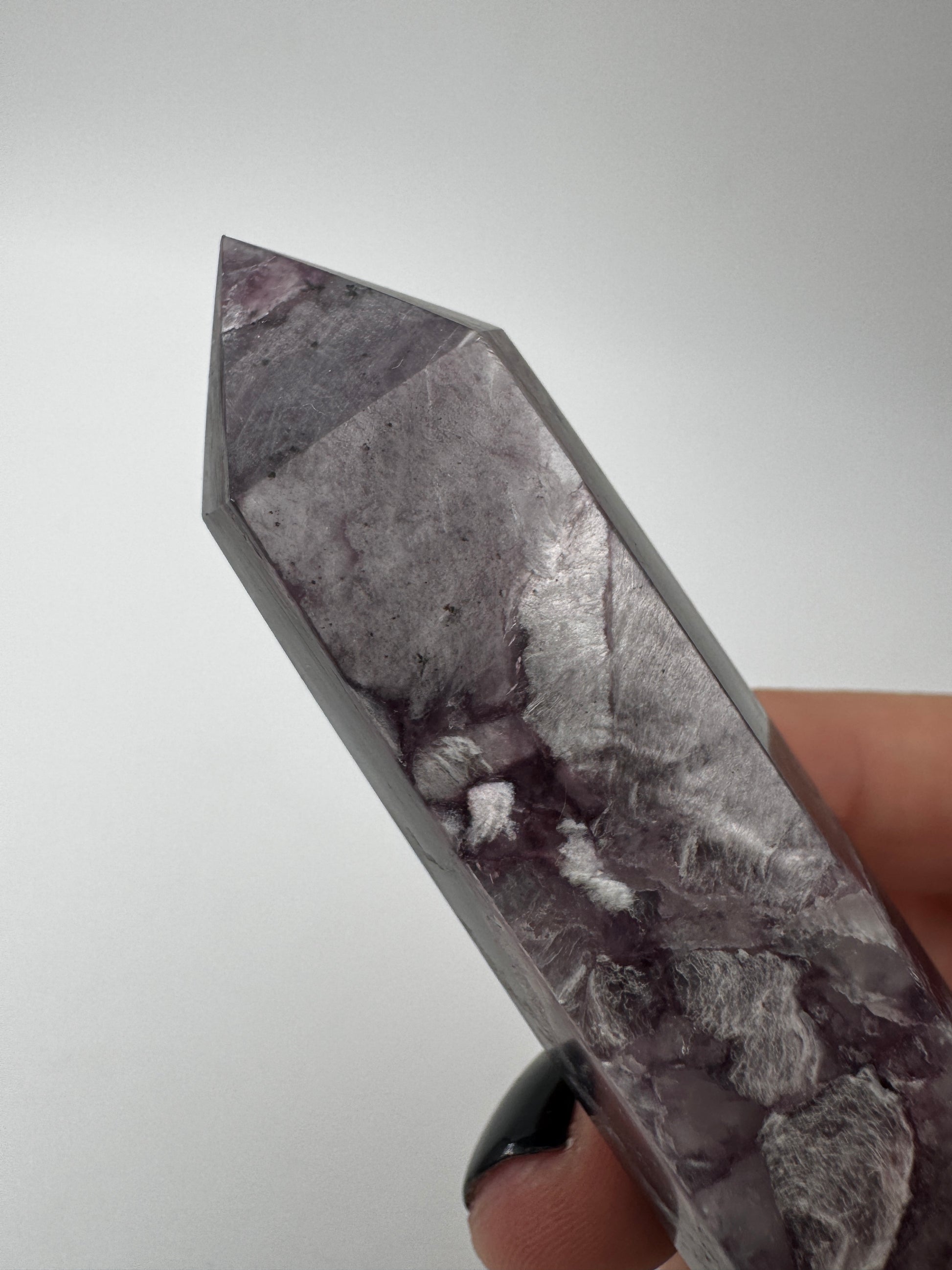Ein spitz zulaufender, polierter Turm aus fliederfarbenem Lepidolith mit dezent glitzernden Glimmer-Einschlüssen