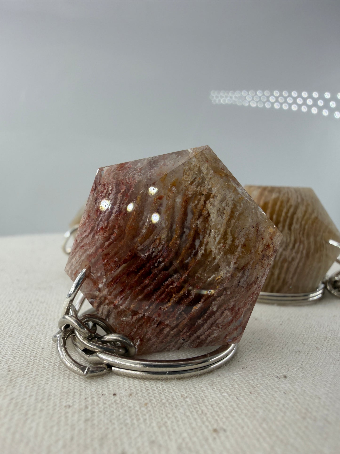 Ein klarer Lodolith-Anhänger in sechseckiger Form mit dichten, schichtartigen Einschlüssen in Erdtönen an einem stabilen Metallring.
