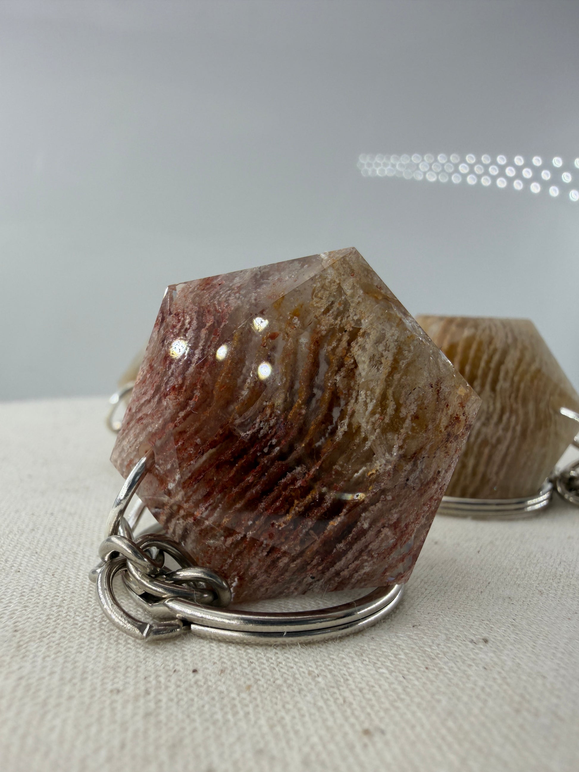Ein klarer Lodolith-Anhänger in sechseckiger Form mit dichten, schichtartigen Einschlüssen in Erdtönen an einem stabilen Metallring.