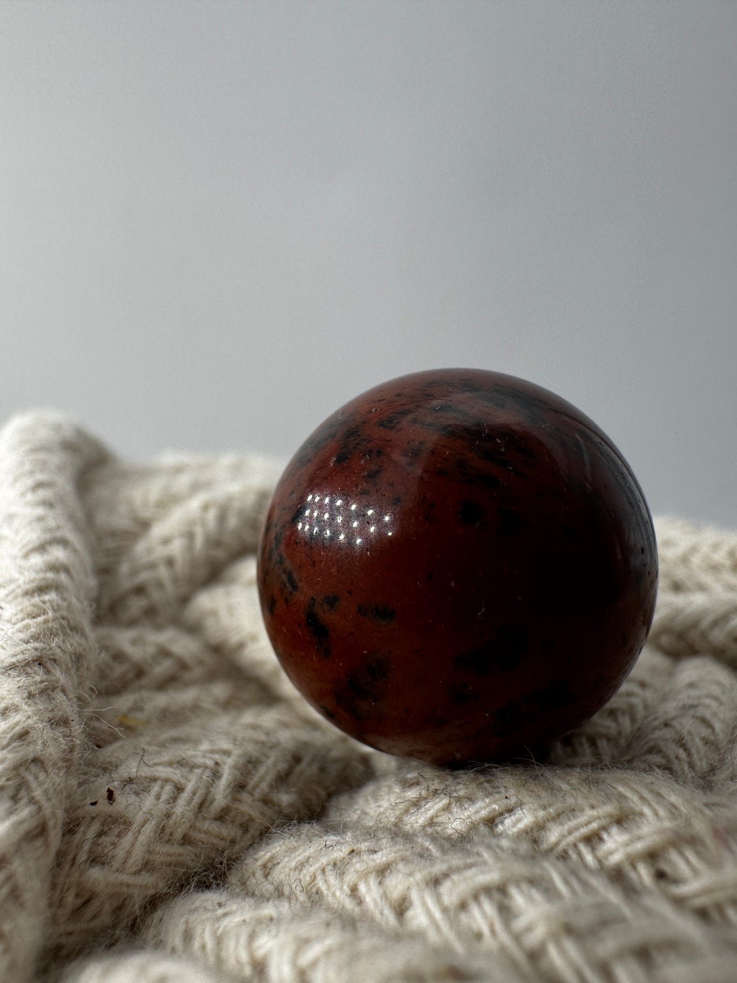 Mehrere hochglanzpolierte Mahagoni-Obsidian Minikugeln mit einer markanten rot-schwarzen Fließtextur, arrangiert auf einer hellen Unterlage.