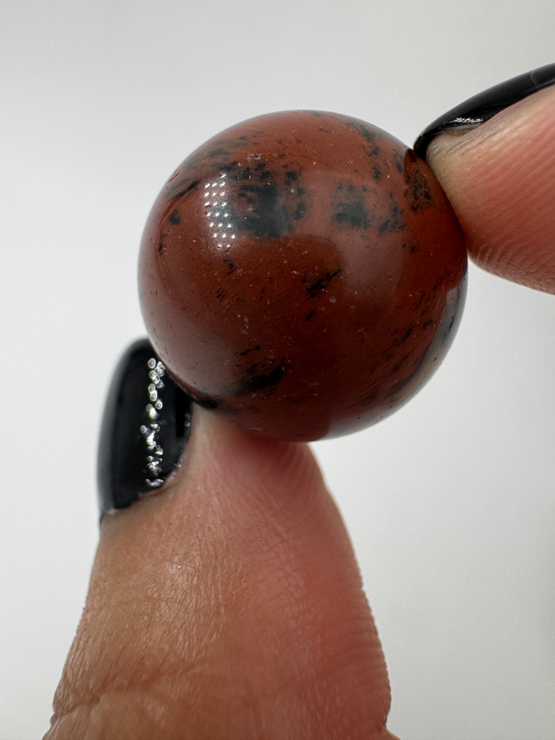 Eine Mahagoni-Obsidian Minikugel mit einer markanten rot-schwarzen Fließtextur.