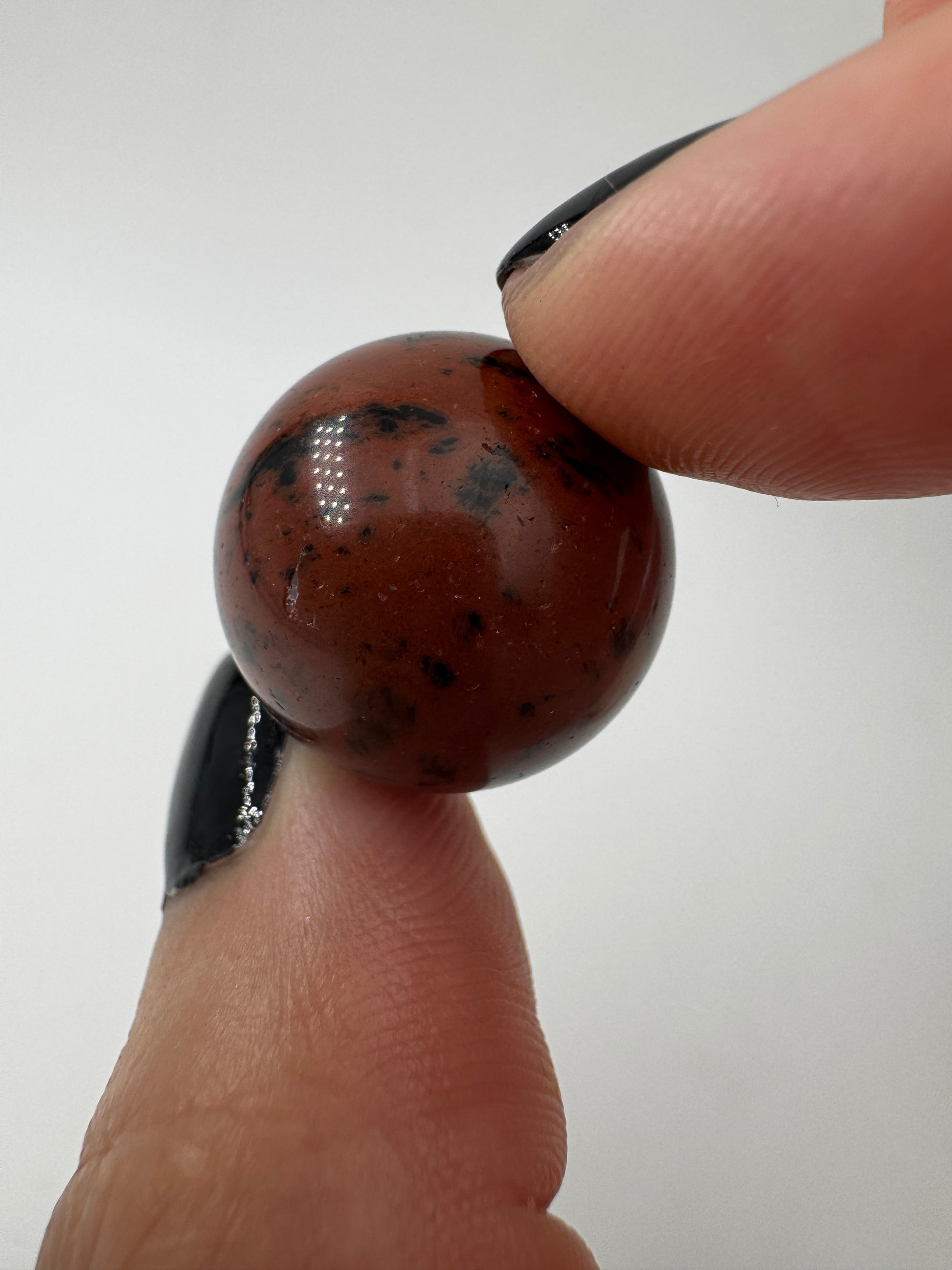 Eine Mahagoni-Obsidian Minikugel mit einer markanten rot-schwarzen Fließtextur.