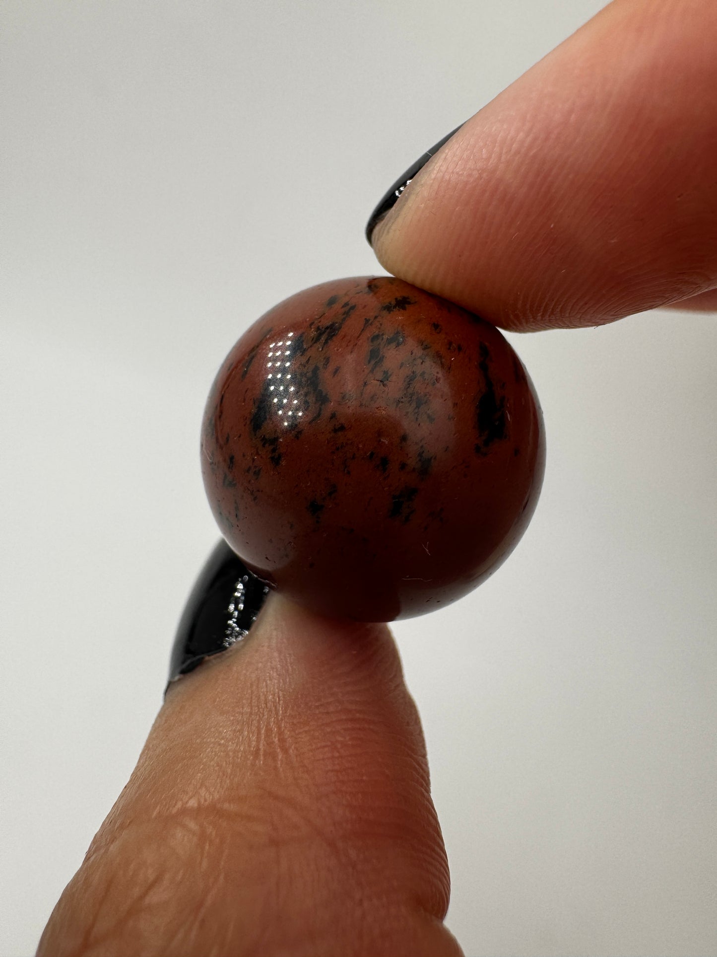 Eine Mahagoni-Obsidian Minikugel mit einer markanten rot-schwarzen Fließtextur.