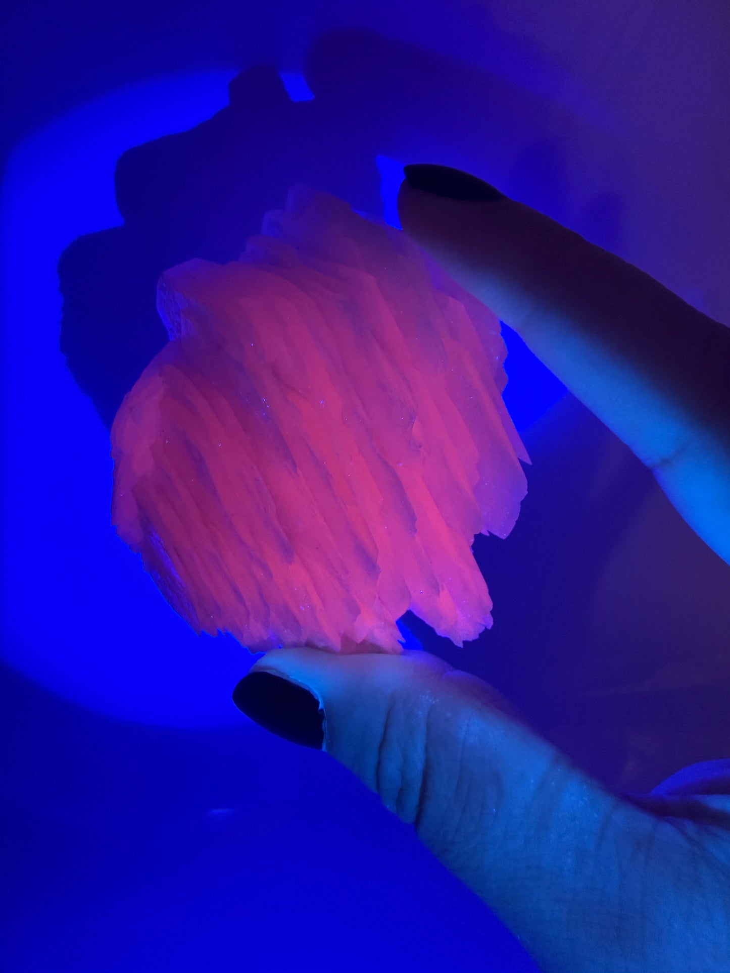 Naturbelassener Rohstein aus Mangano-Calcit in zartem Rosa mit sichtbaren Spaltflächen unter UV-Licht.