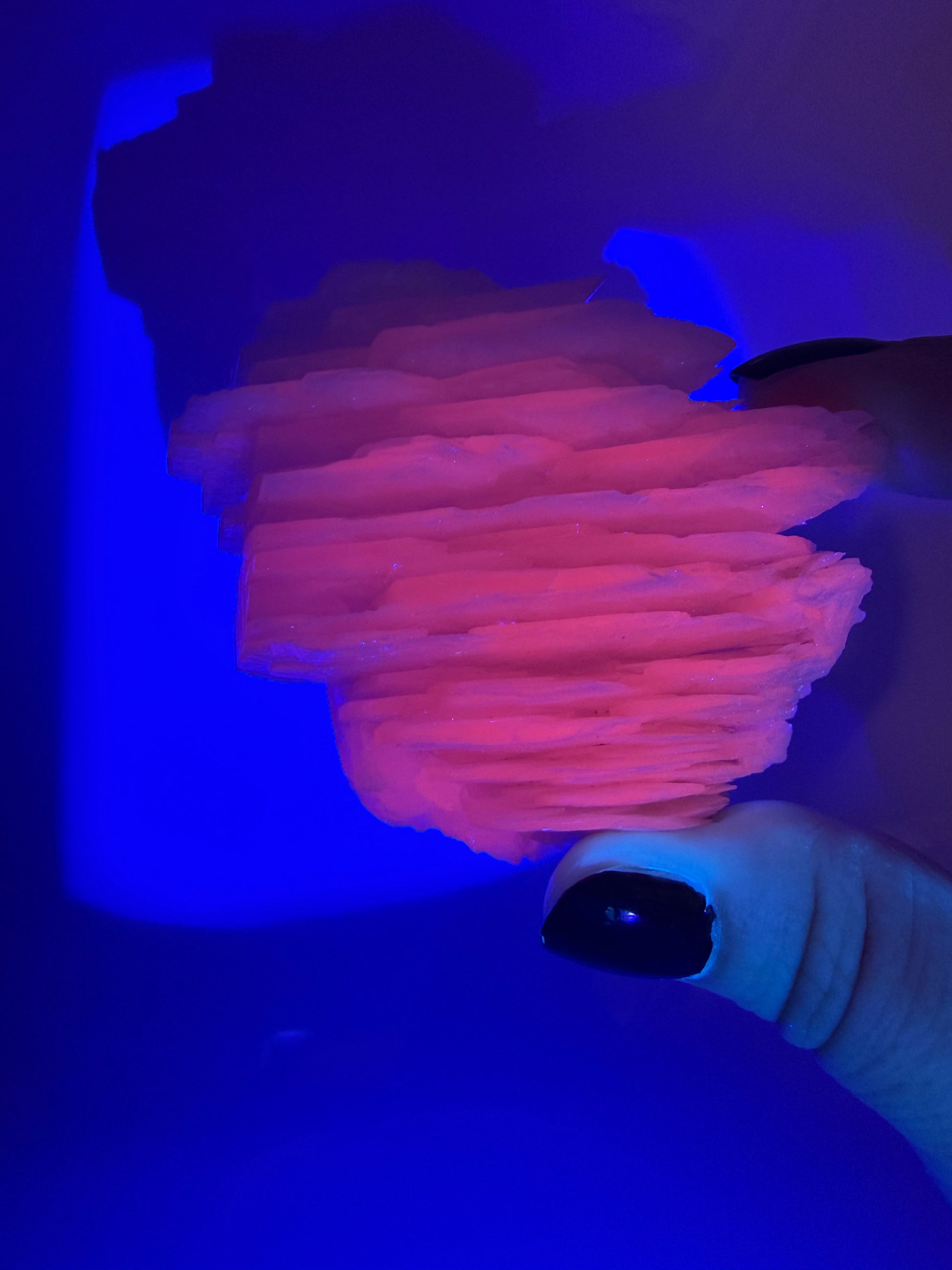 Naturbelassener Rohstein aus Mangano-Calcit in zartem Rosa mit sichtbaren Spaltflächen unter UV-Licht.