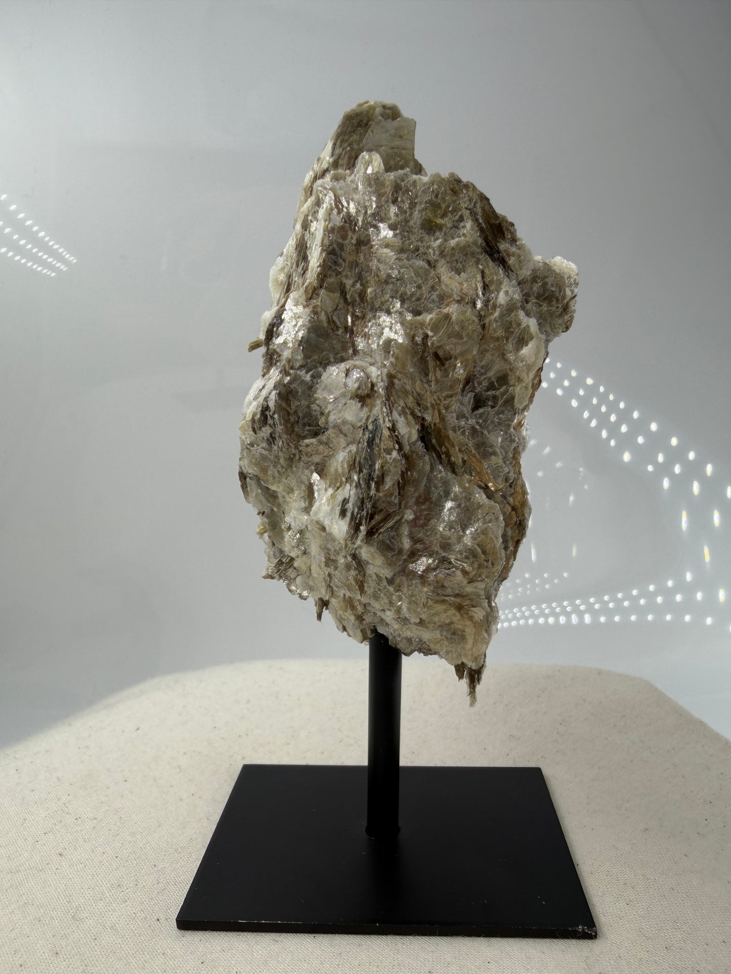 Silbrig glänzender Muskovit-Glimmer auf einem schwarzen Metallständer zur dekorativen Präsentation.