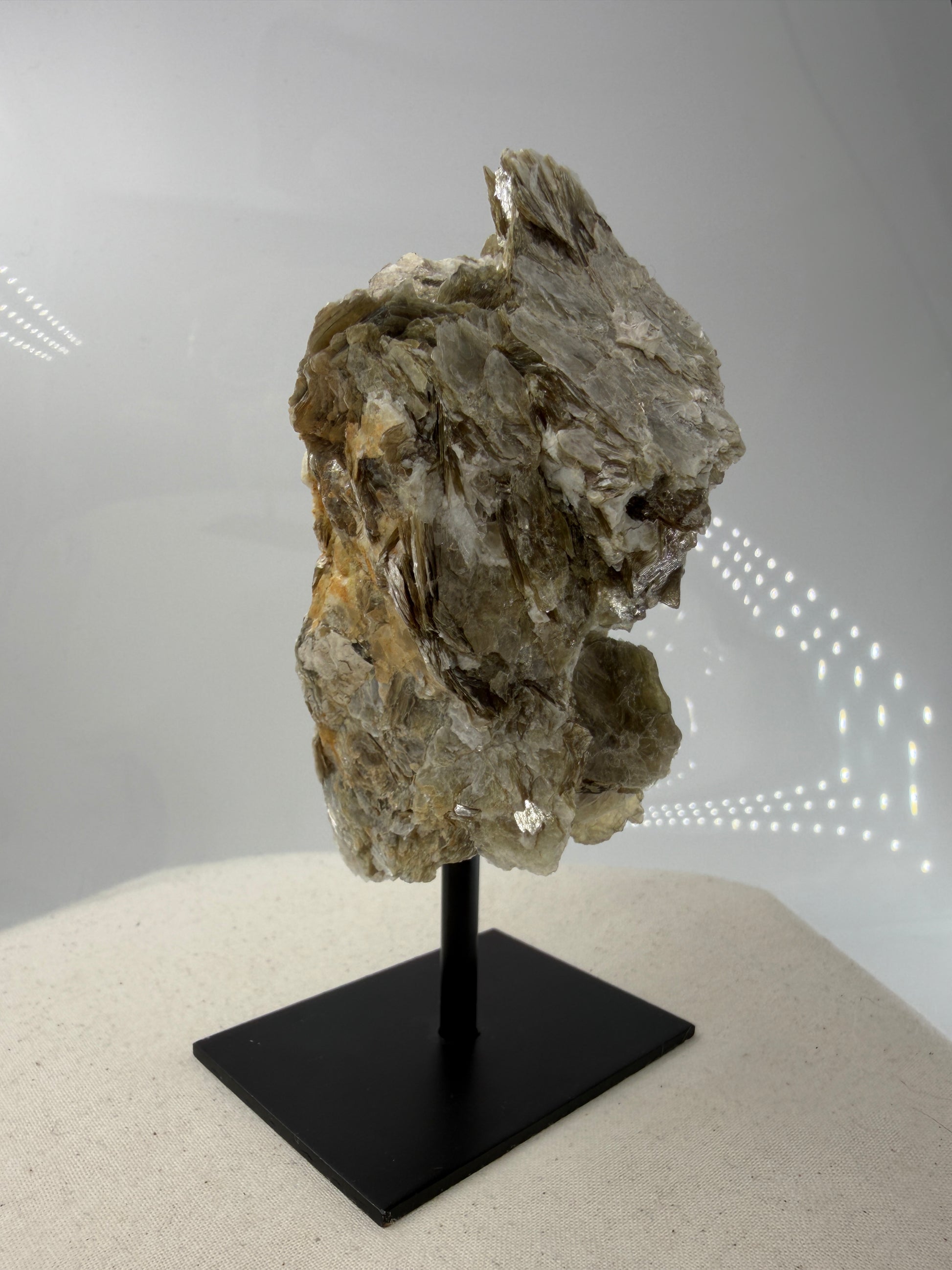 Silbrig glänzender Muskovit-Glimmer auf einem schwarzen Metallständer zur dekorativen Präsentation.
