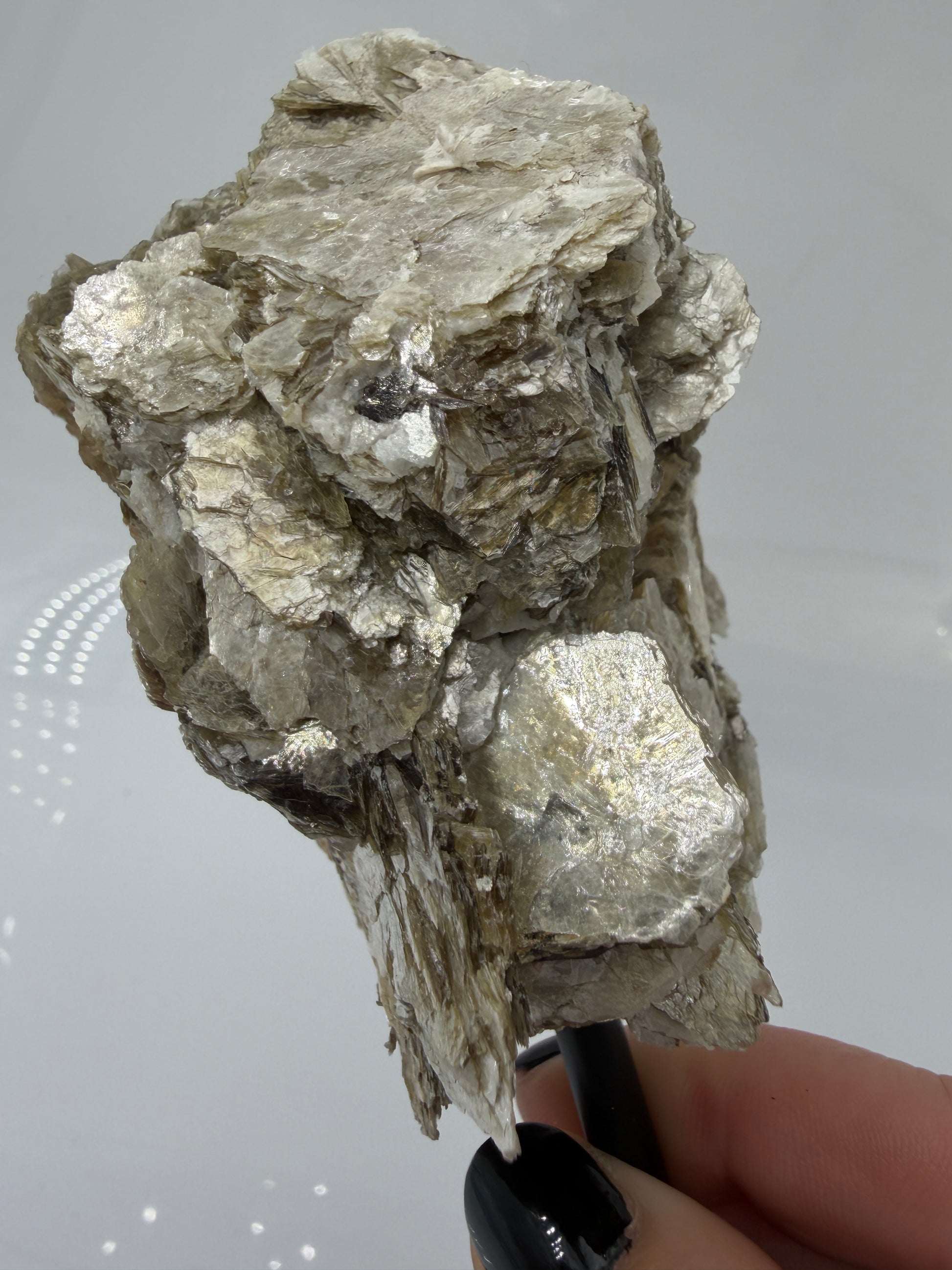 Silbrig glänzender Muskovit-Glimmer auf einem schwarzen Metallständer zur dekorativen Präsentation.