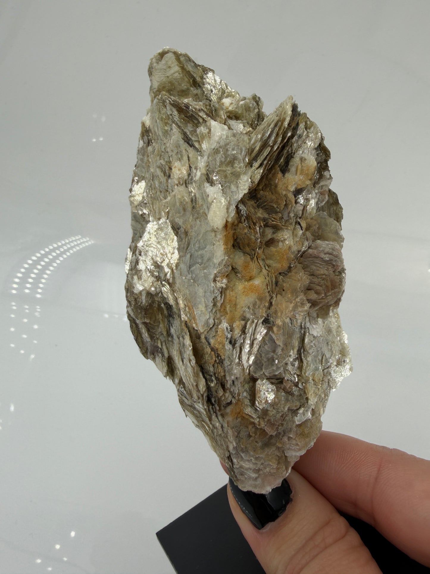 Silbrig glänzender Muskovit-Glimmer auf einem schwarzen Metallständer zur dekorativen Präsentation.