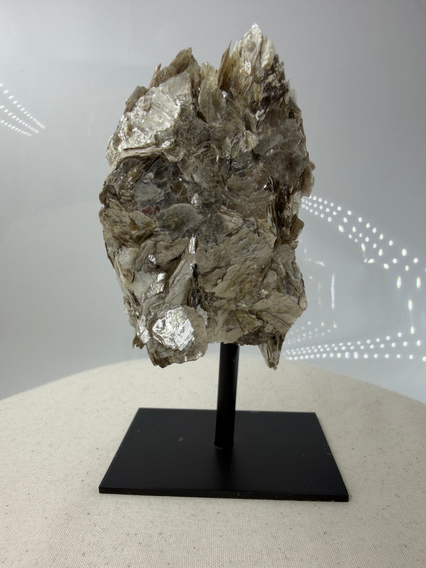 Silbrig glänzender Muskovit-Glimmer auf einem schwarzen Metallständer zur dekorativen Präsentation.